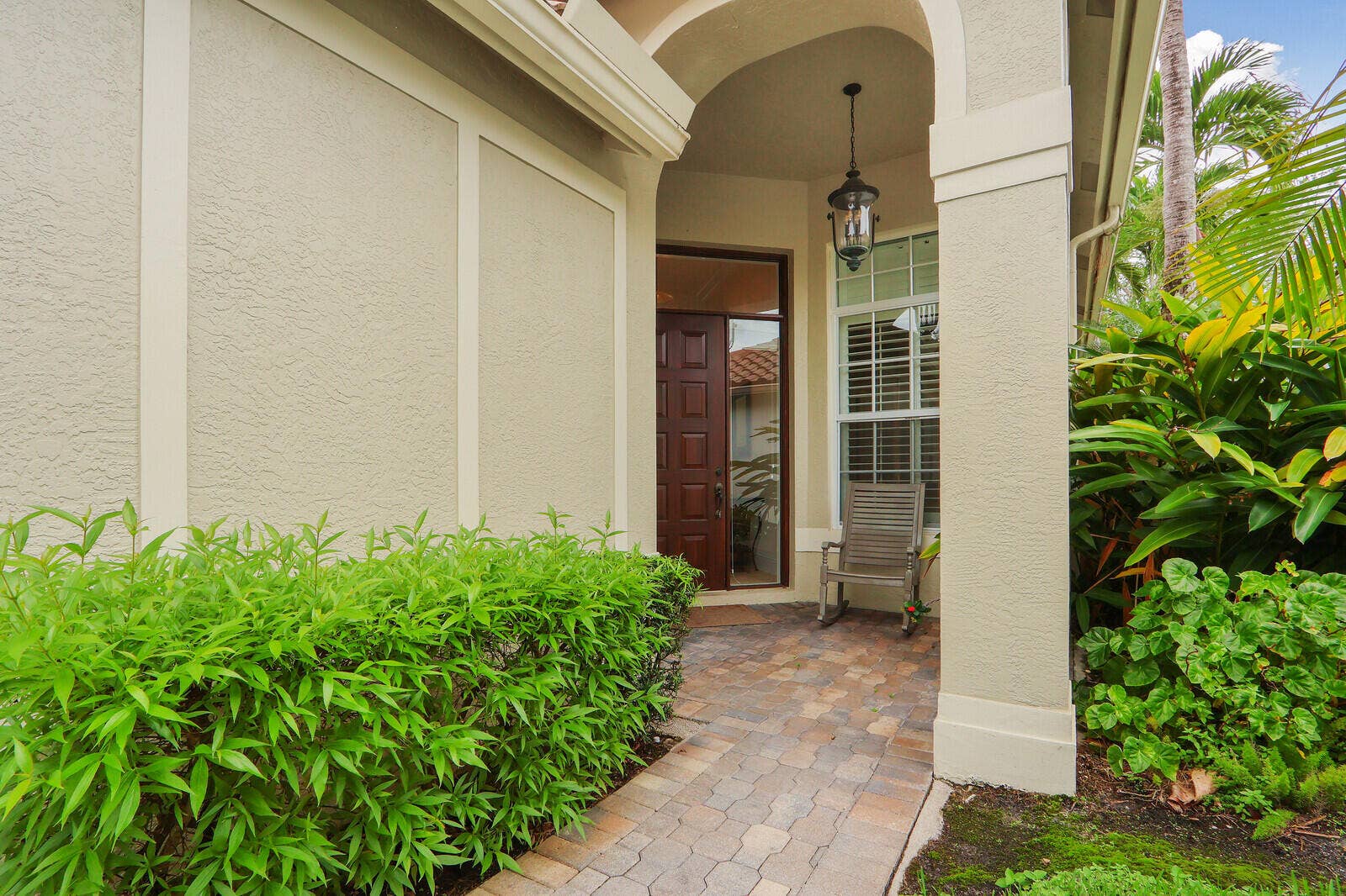 Arched entry with a wood-paneled door, paver walkway, stucco exterior, and mature landscaping