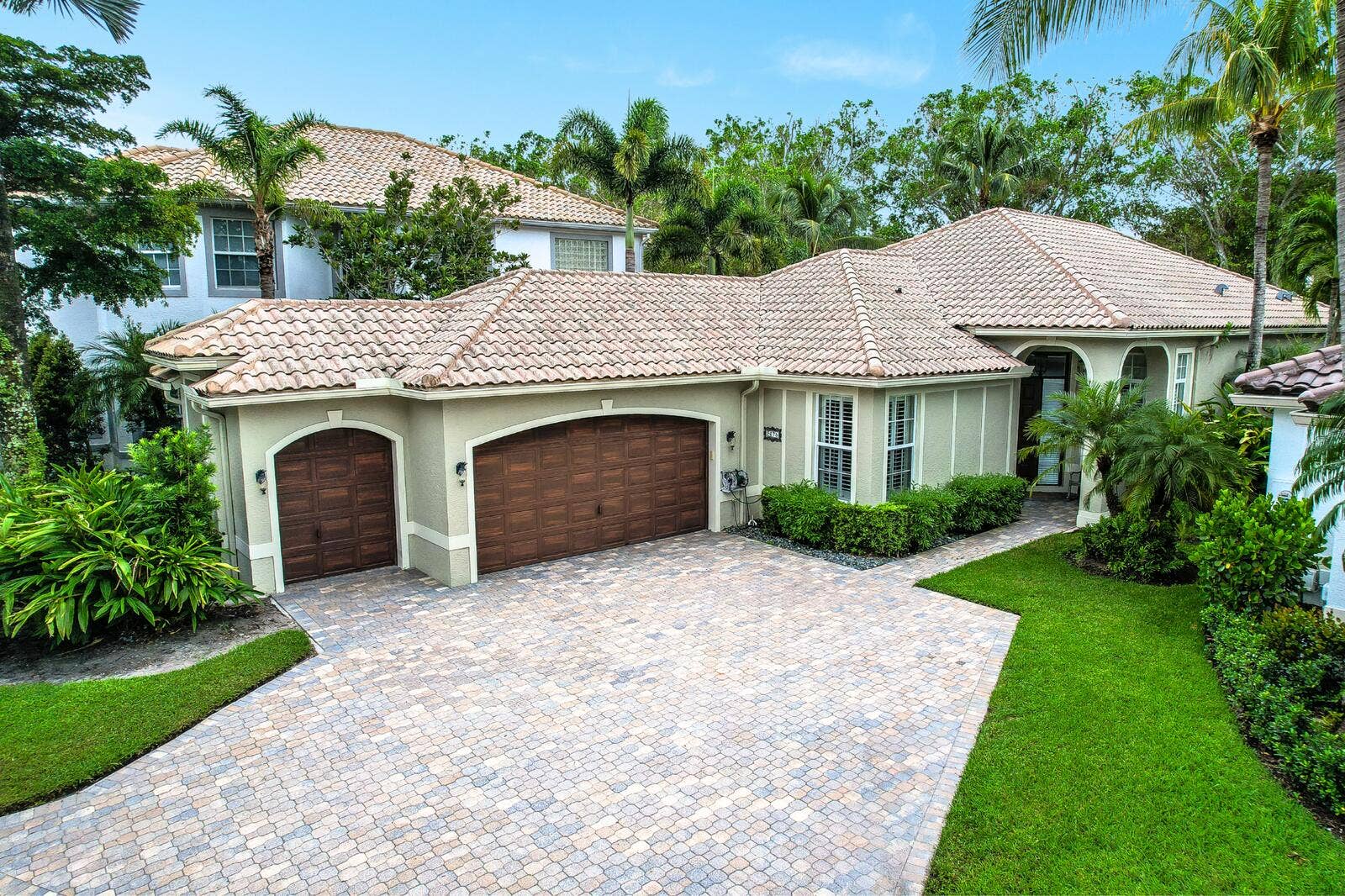 Tile roof, stucco exterior, arched garage doors, paver driveway, and mature landscaping