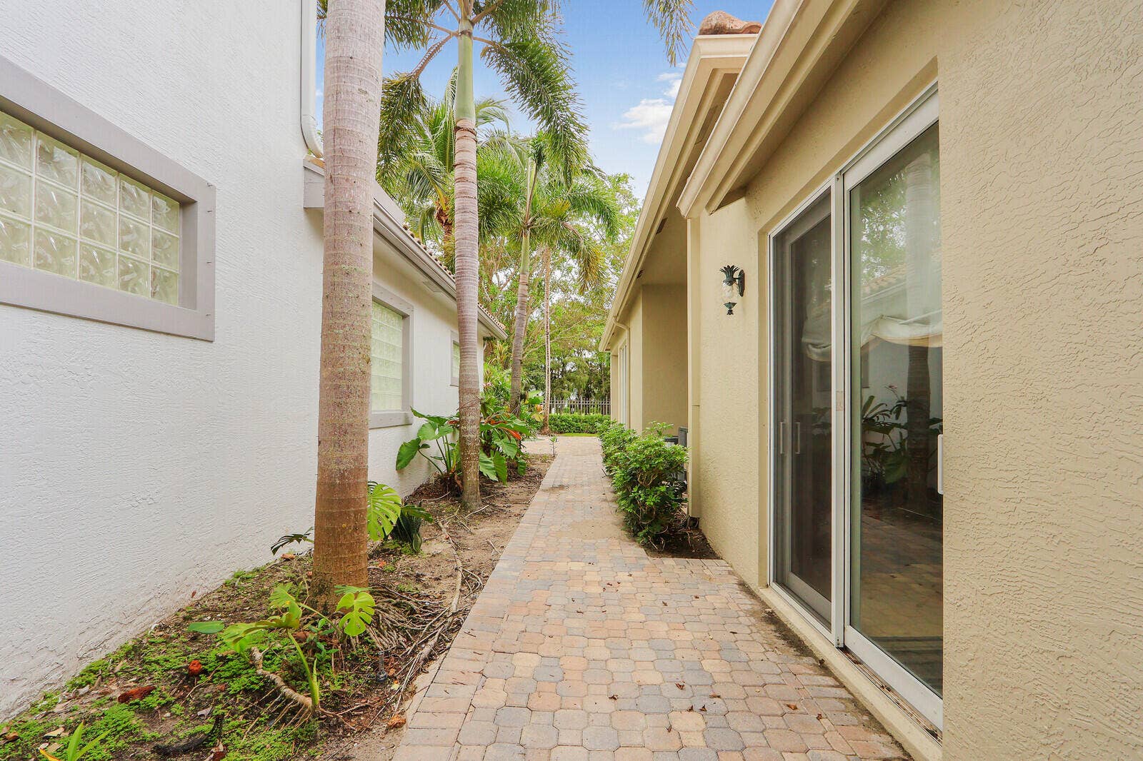 Paver walkway, mature palm trees, glass block window, sliding glass door, exterior wall sconce