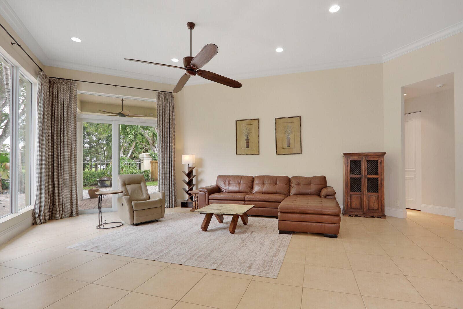 Spacious living area featuring tile flooring, expansive impact windows throughout, recessed lighting, and ceiling fans