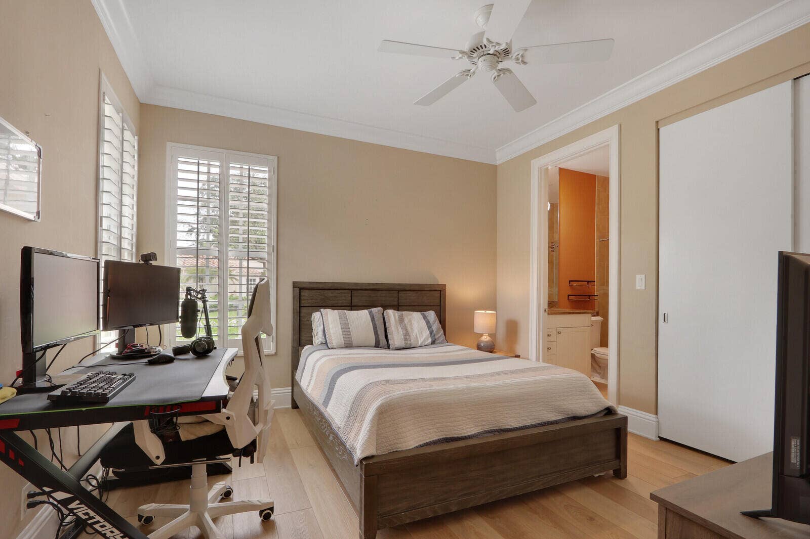 Wood-finish flooring with crown molding, plantation shutters, built-in closet with sliding doors, and a ceiling fan