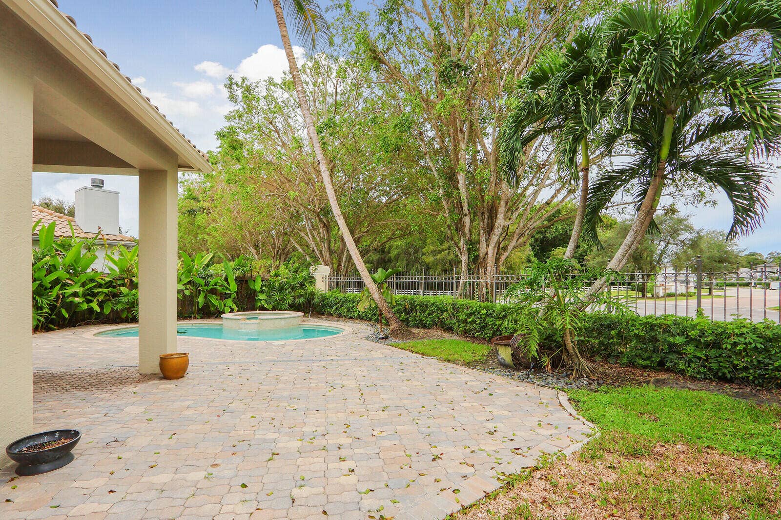 Paved patio featuring a round pool with an integrated spa, mature palm trees, and lush landscaping