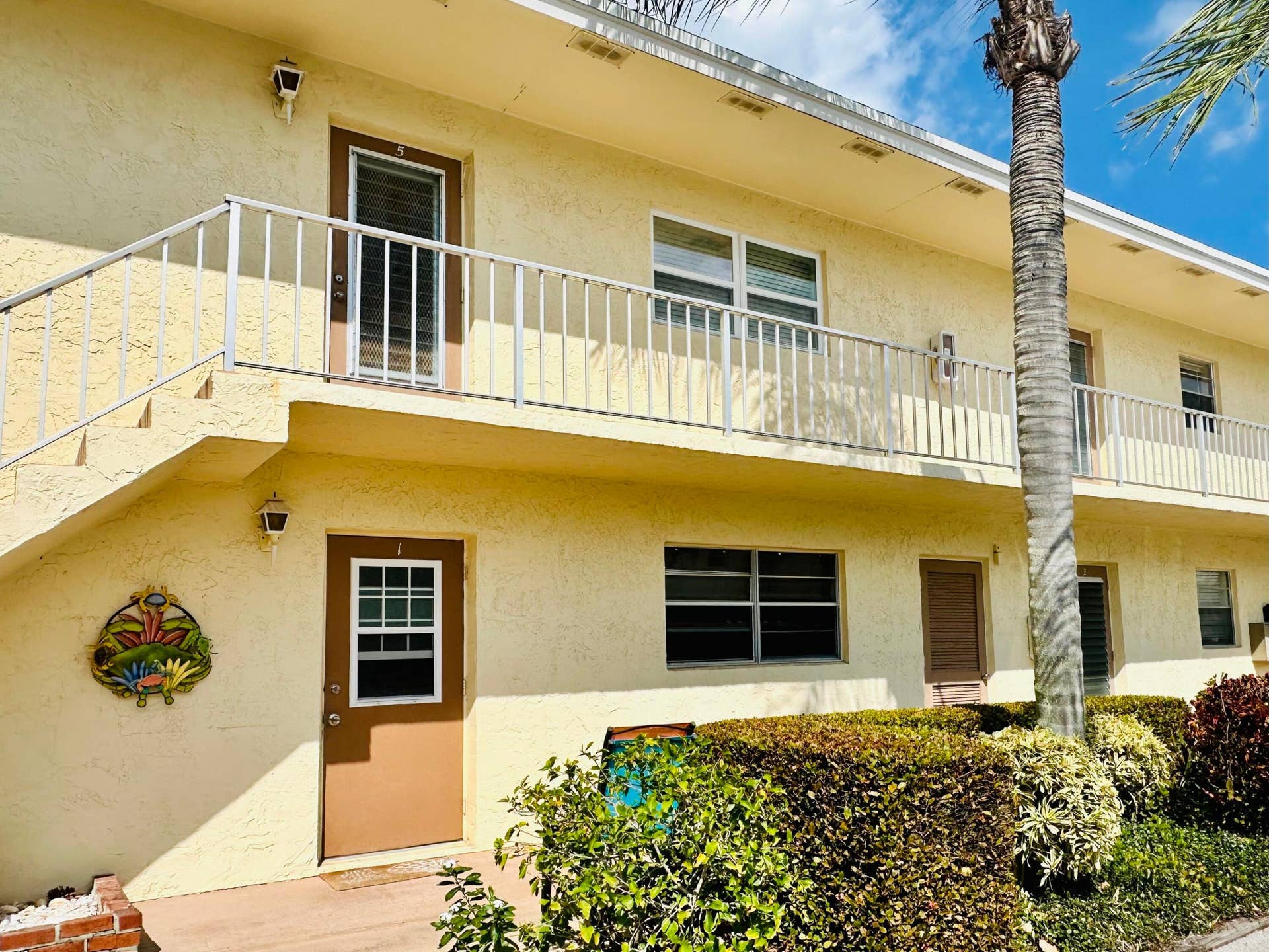 2950 SE Ocean Boulevard, #130-6, Stuart, FL 34996 Two-story building with textured stucco exterior, white railings, exterior lighting fixtures, and ground-level plantings