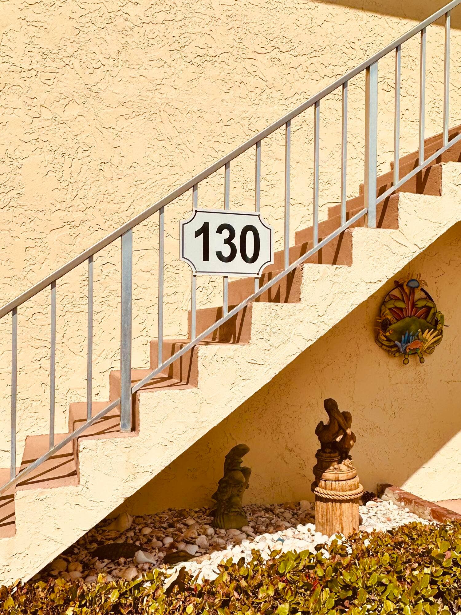 2950 SE Ocean Boulevard, #130-6, Stuart, FL 34996 Staircase featuring metal railings, textured stucco exterior, and a decorative house number plaque