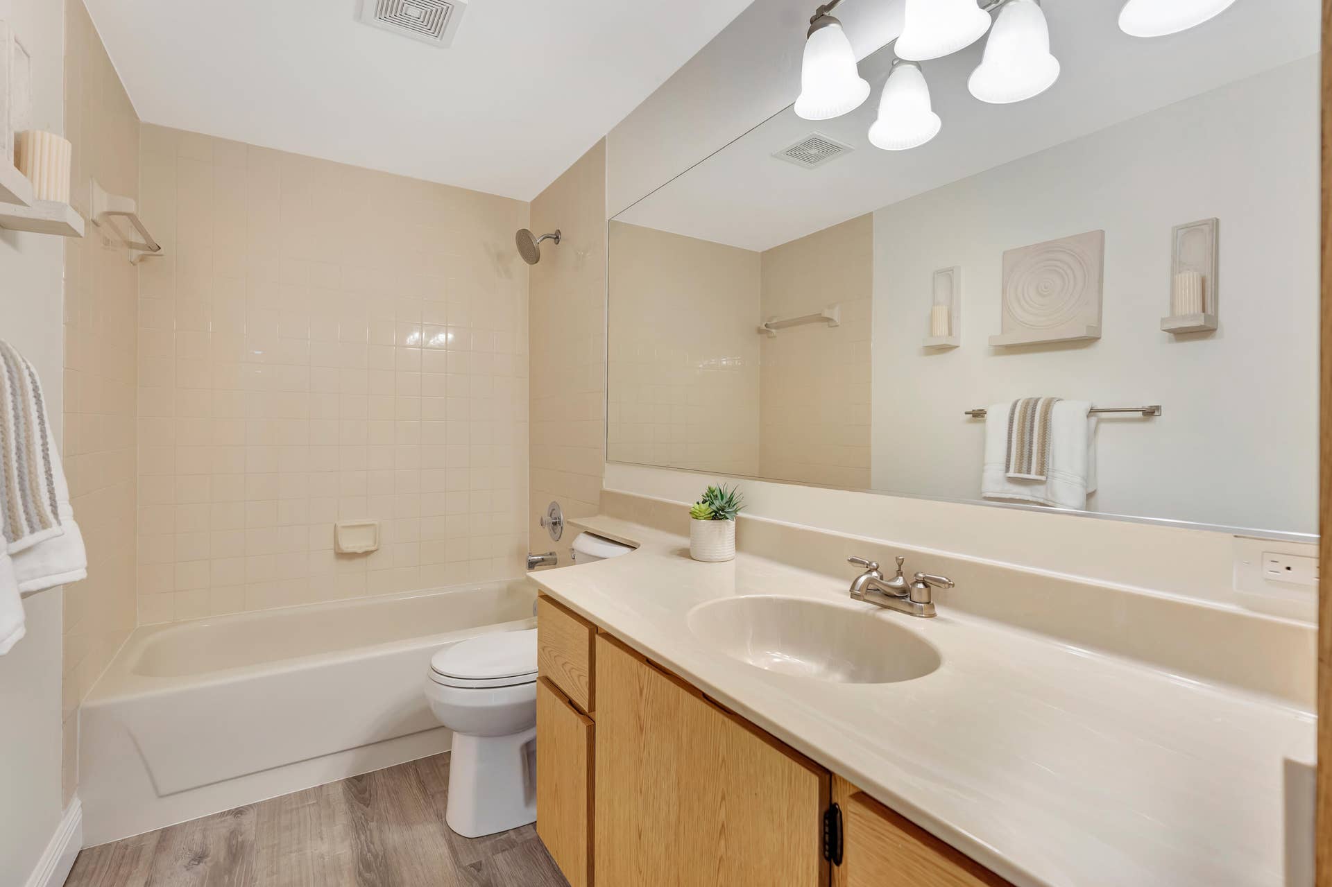 Full vanity mirror, wood-finish flooring, light-toned tile shower surround, and a vanity with an integrated sink