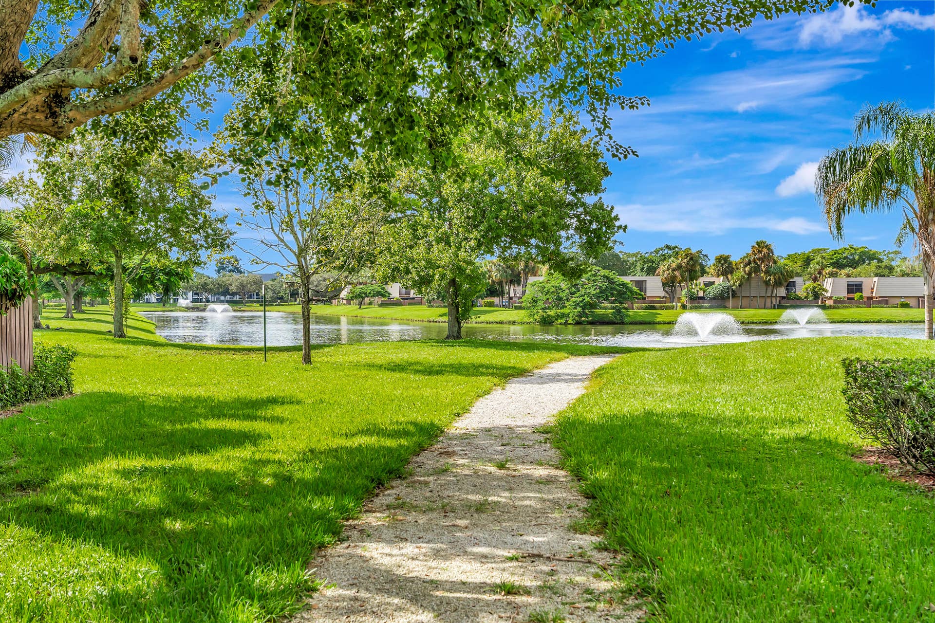 Manicured lawn with mature trees and a gravel pathway leading to a body of water with fountains