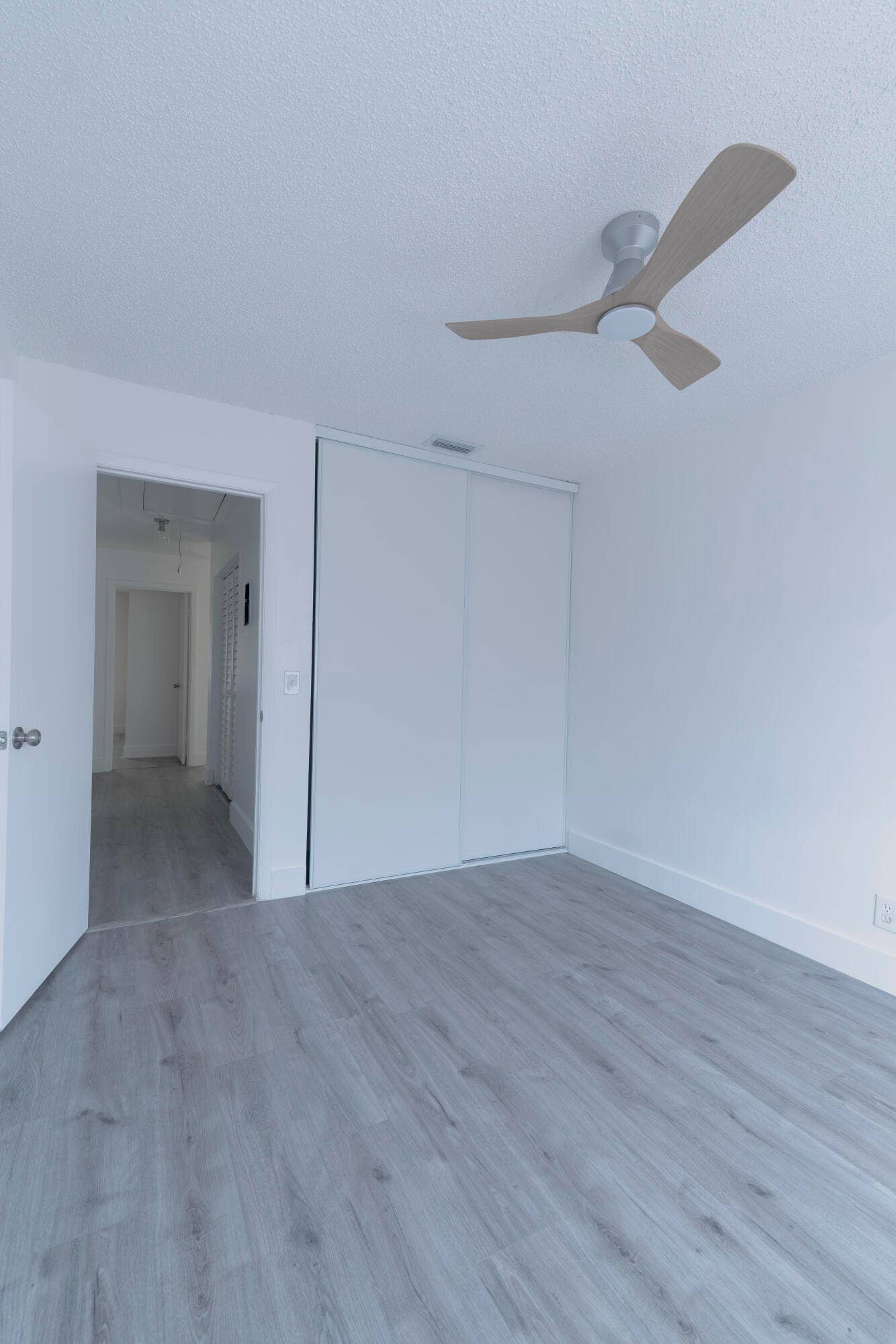 vinyl wood like flooring throughout, bright white walls, contemporary ceiling fan, and sliding closet doors