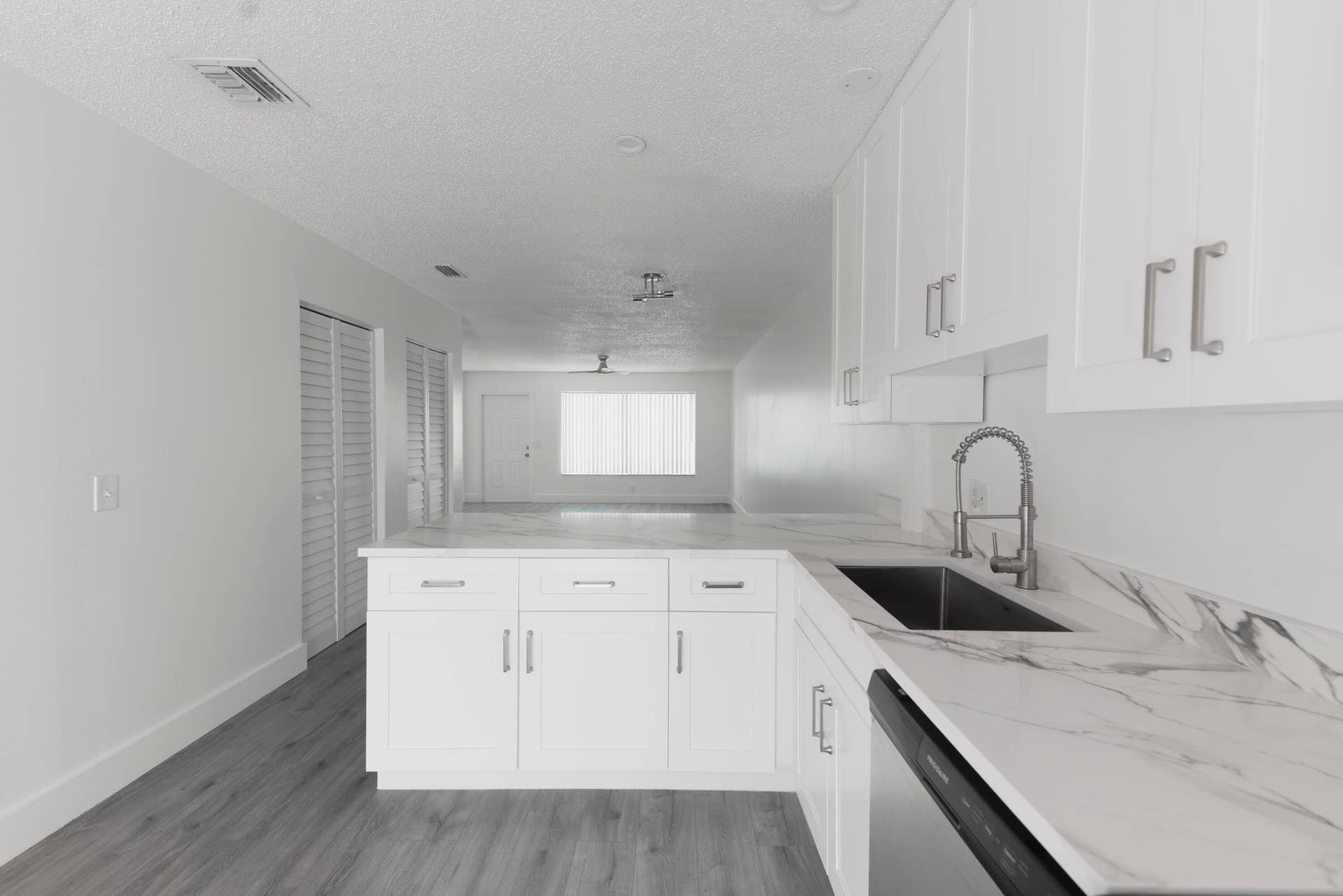 White shaker cabinetry, stone-finish countertops, stainless steel sink, pull-down sprayer faucet, and vinyl wood like flooring