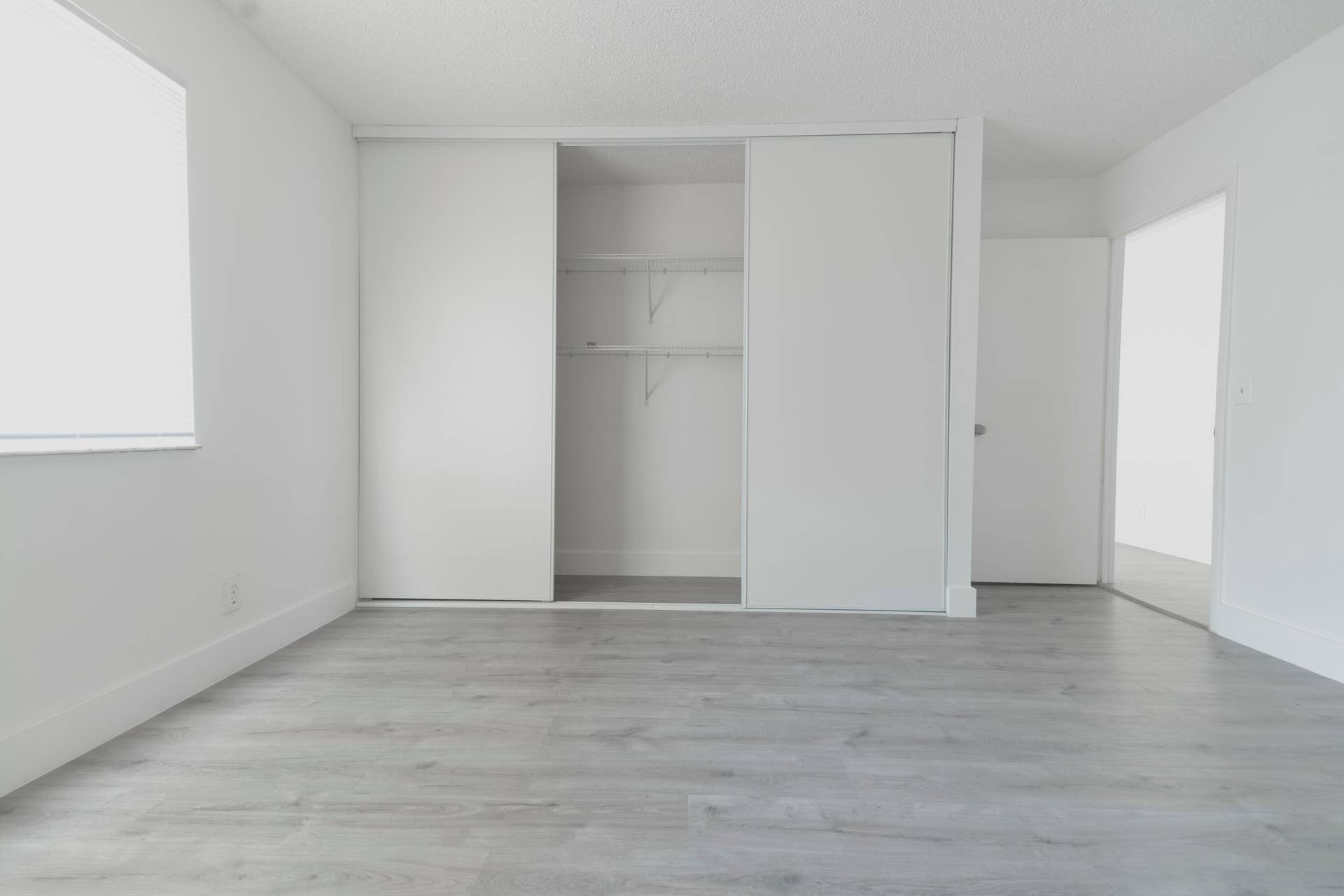 Light vinyl wood like flooring, white walls, and a sliding closet door with wire shelving