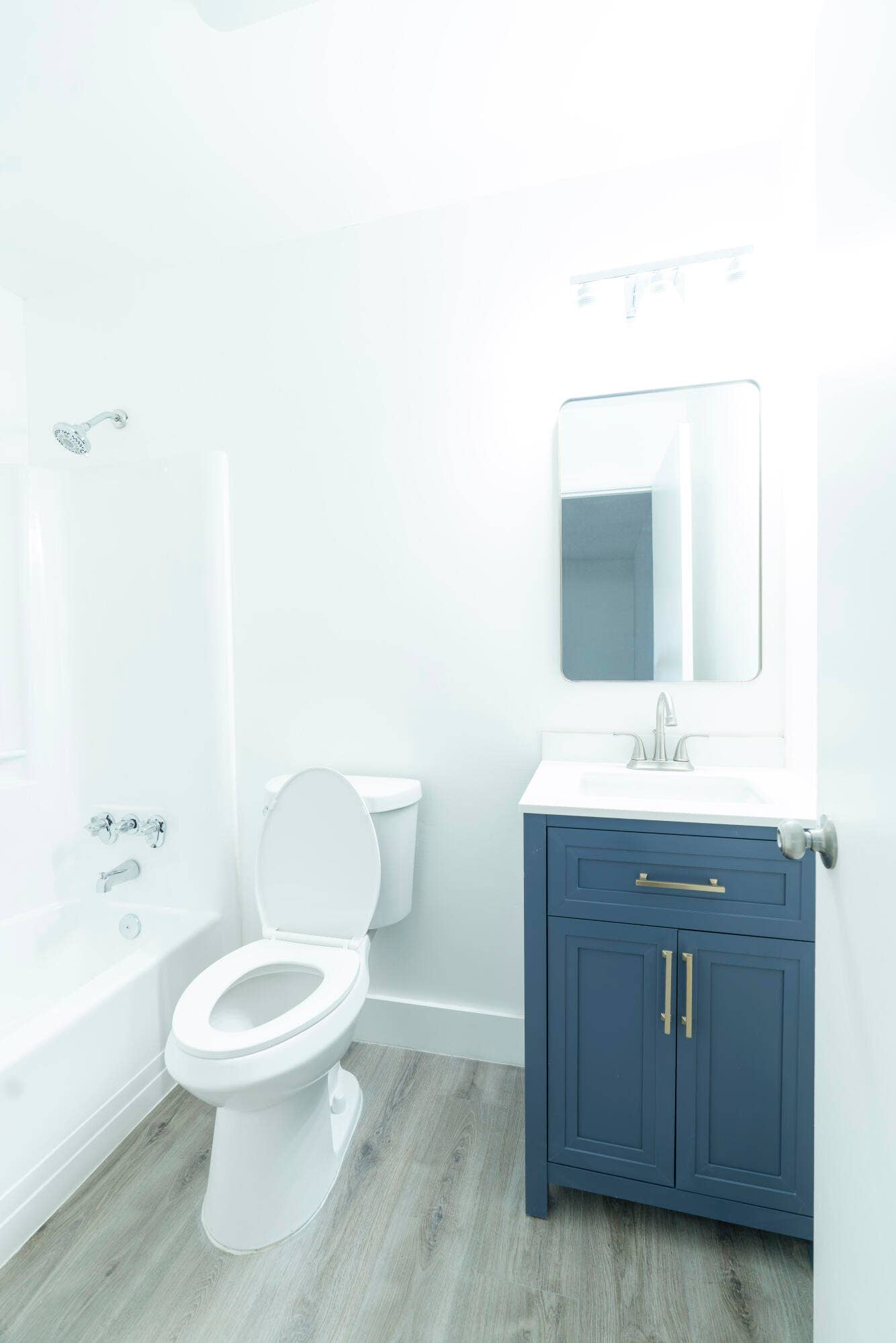Bathroom featuring a white toilet, white bathtub and shower combination, blue vanity with an integrated white sink, chrome faucet, and vinyl wood like flooring