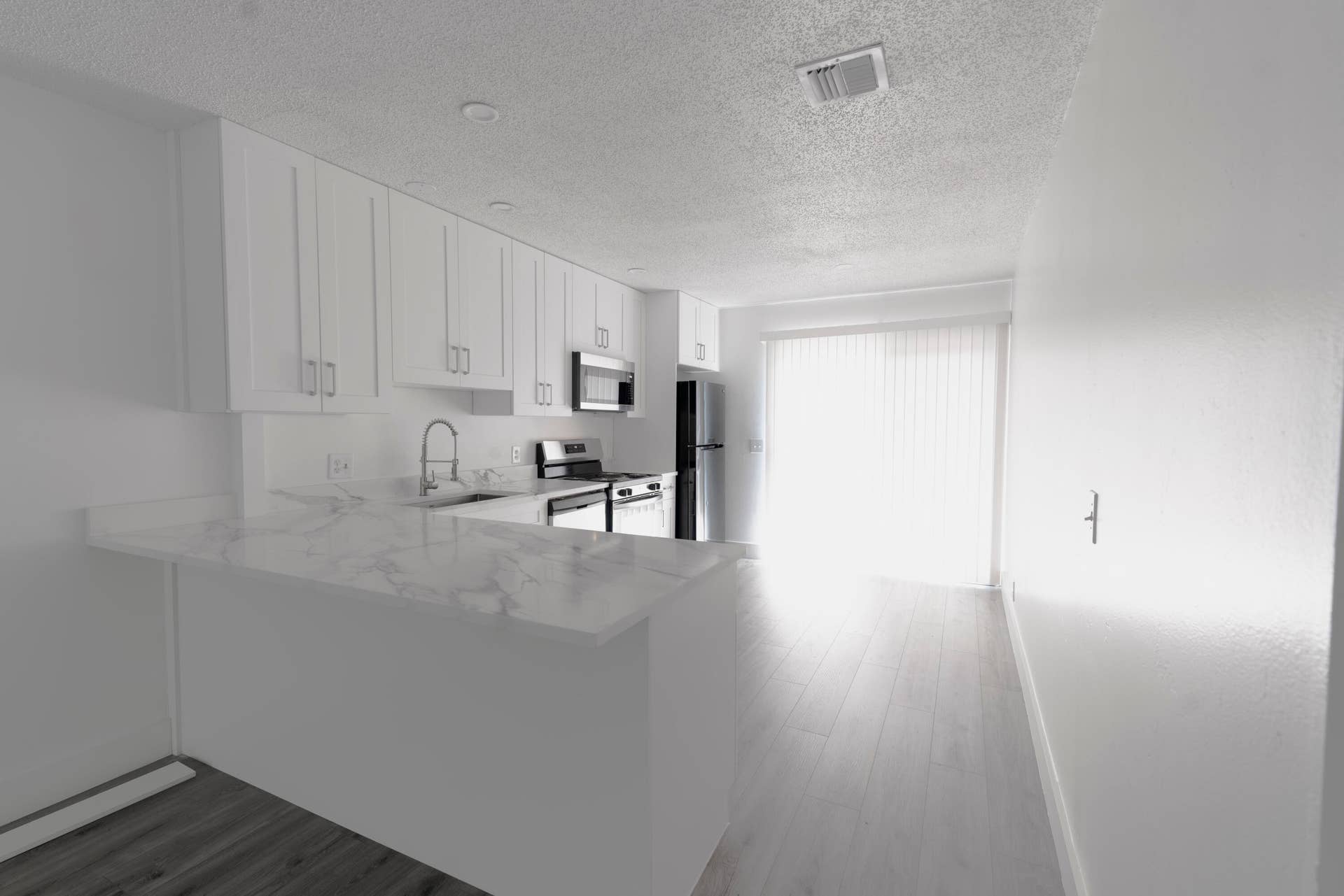 Kitchen featuring white cabinetry, a waterfall-edge countertop, stainless steel appliances, and vinyl wood like flooring