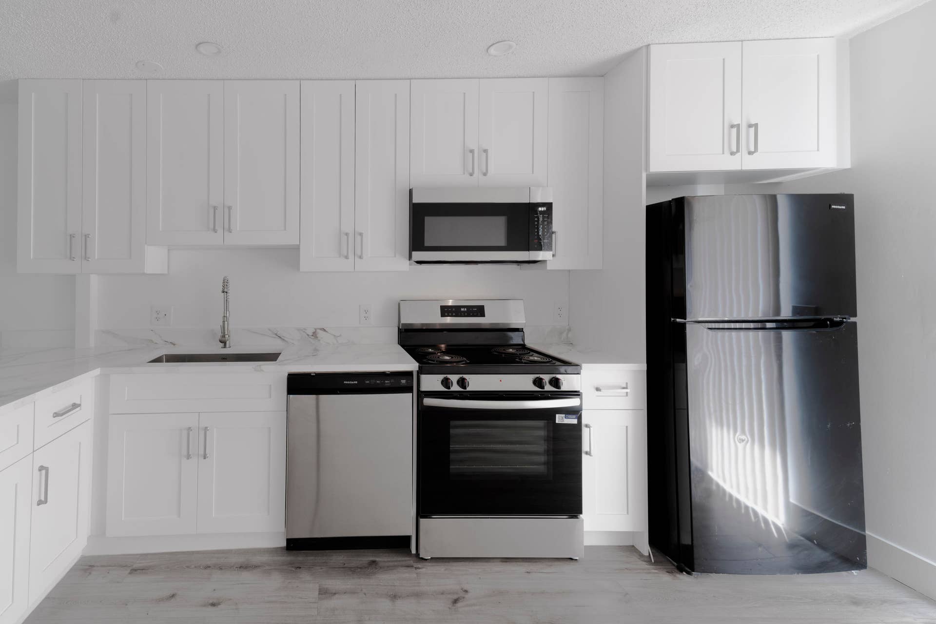 Kitchen featuring white shaker cabinetry, stainless steel appliances, stone countertops, and vinyl wood like flooring