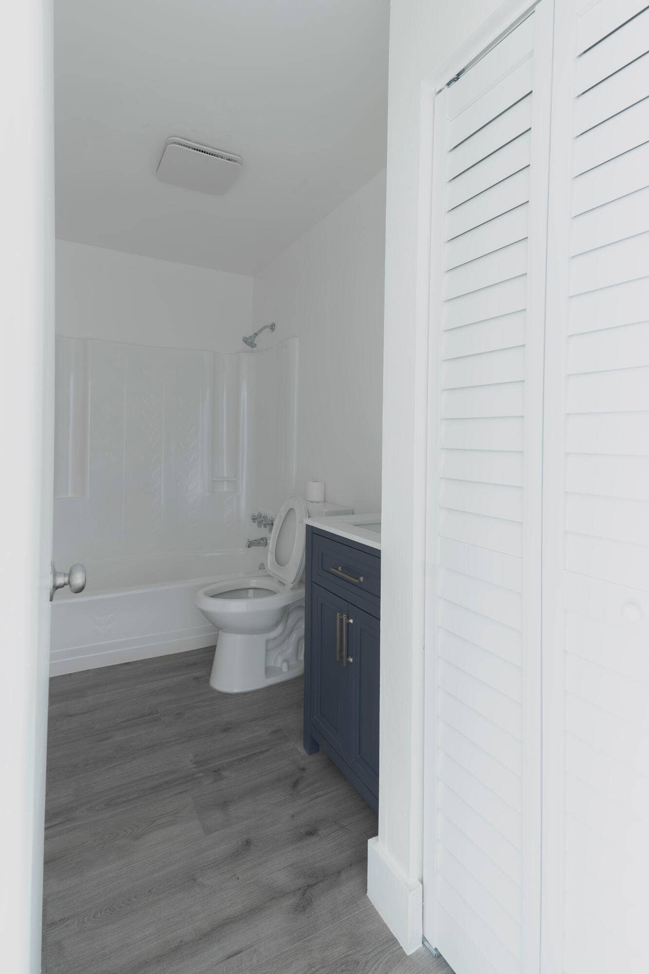 vinyl wood like flooring, white tub with shower, blue vanity with white countertop, and louvered bifold doors
