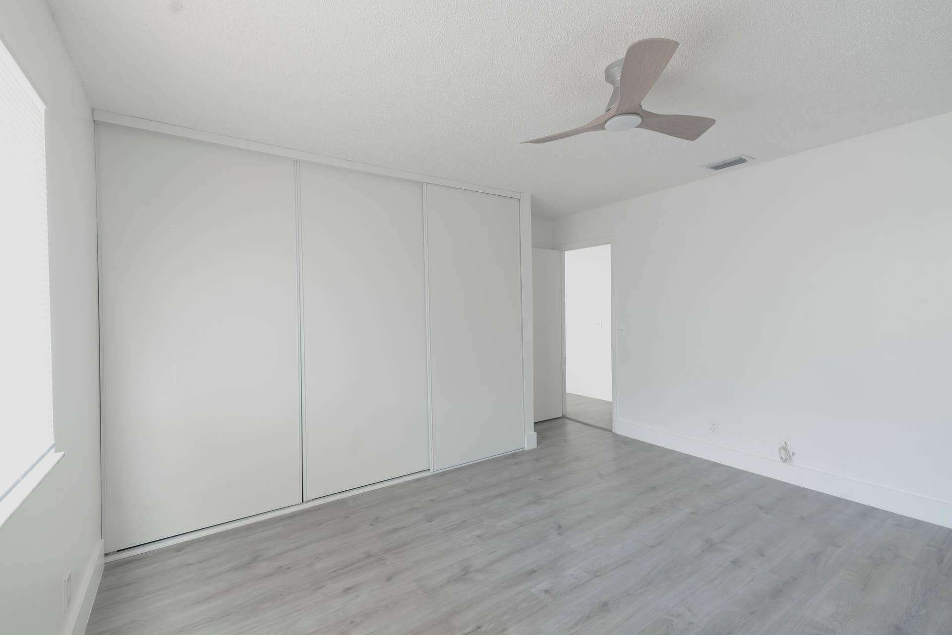 Expansive room with vinyl wood like flooring, a contemporary ceiling fan, and full-wall sliding closet doors