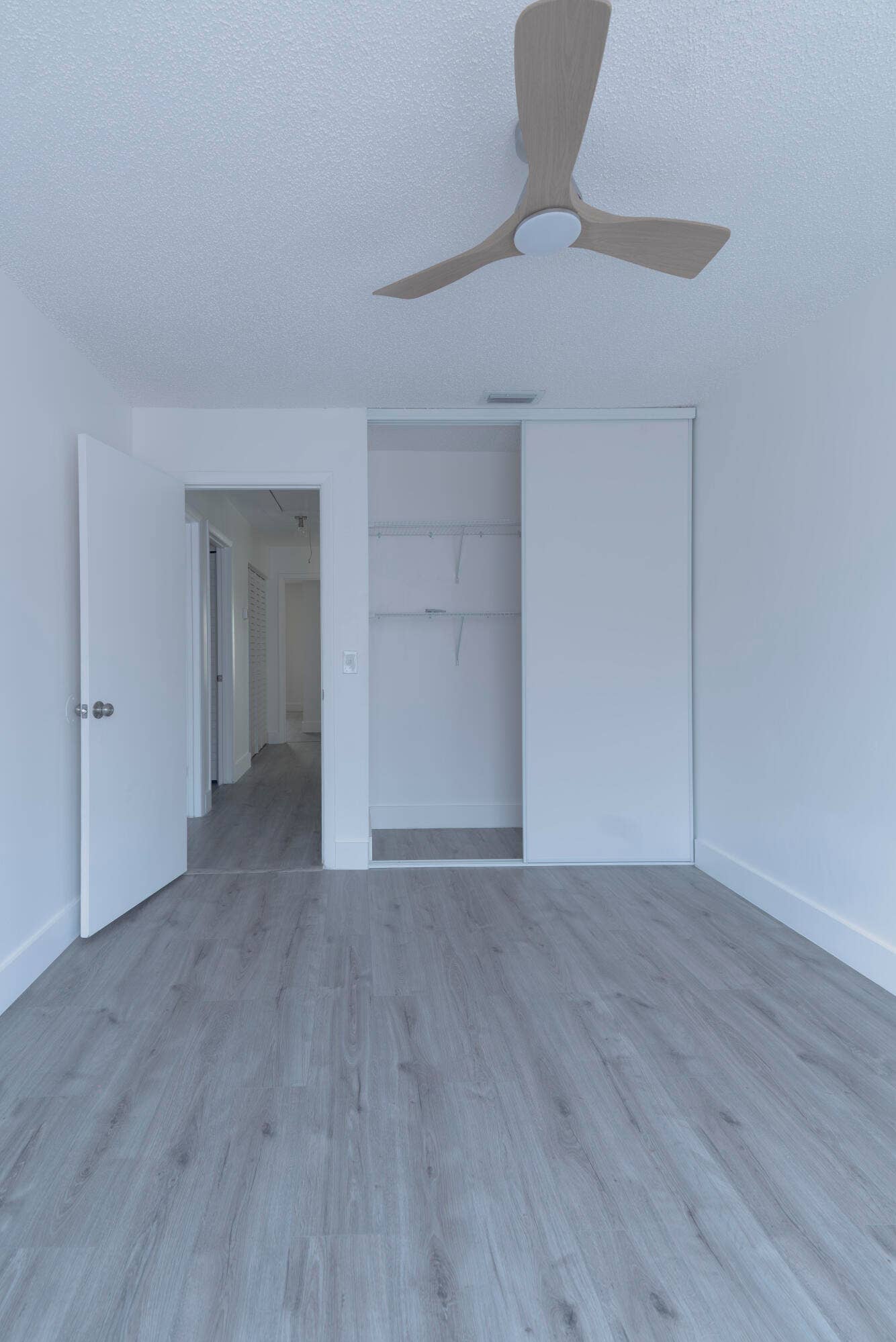 vinyl wood like flooring with white walls, a built-in closet with sliding doors, and a ceiling fan with integrated lighting