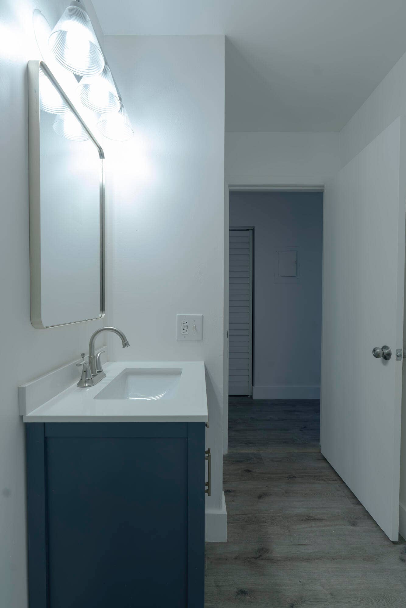 Vanity with white countertop and integrated sink, chrome faucet, wall-mounted mirror, and overhead vanity lighting