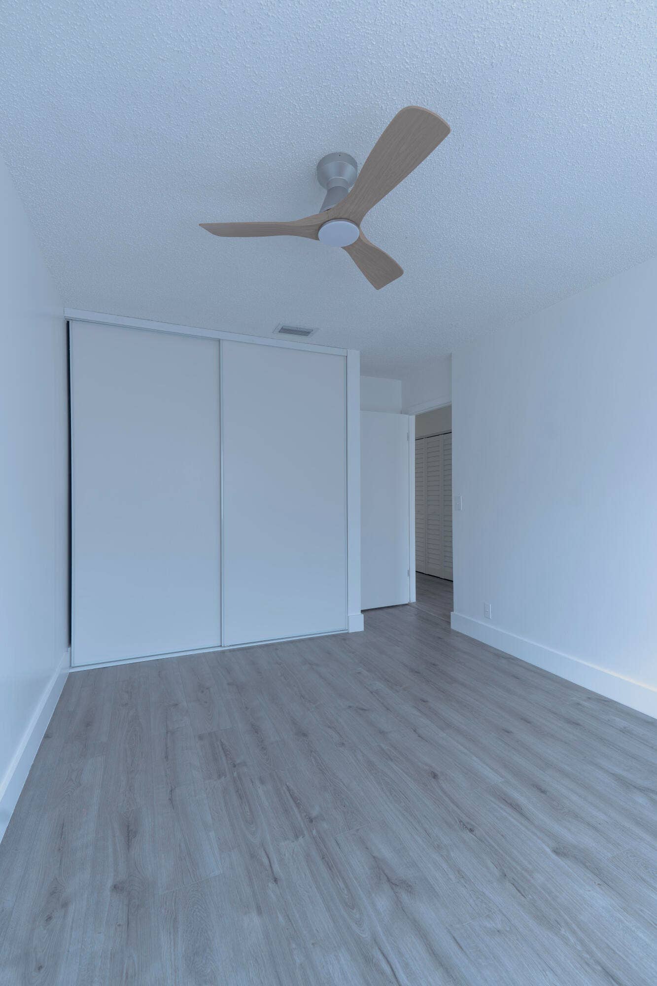 vinyl wood like flooring with a light tone, white walls, and a ceiling fan with light wood-tone blades