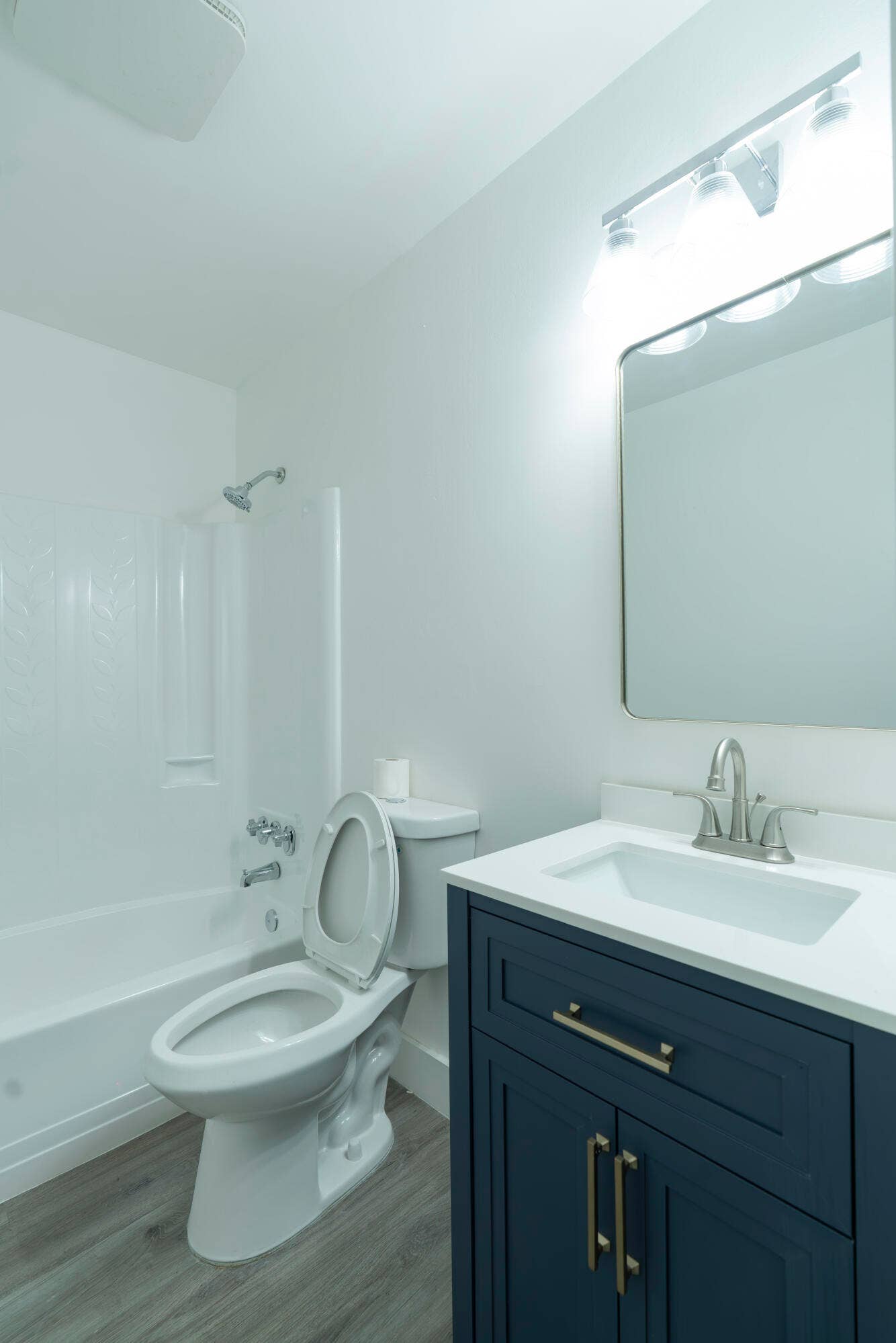 Bathroom featuring a white bathtub, dark blue vanity with gold-tone hardware, white countertop with integrated sink, and vinyl flooring