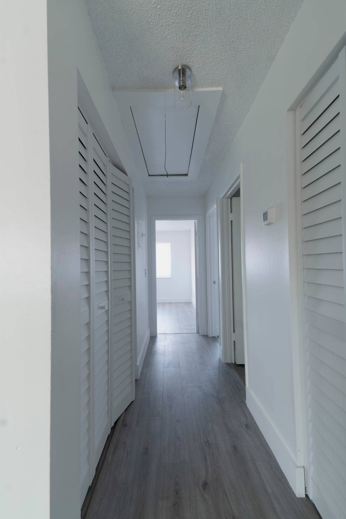 Hallway featuring vinyl flooring, white louvered bifold doors, white painted walls, and a ceiling-mounted light fixture