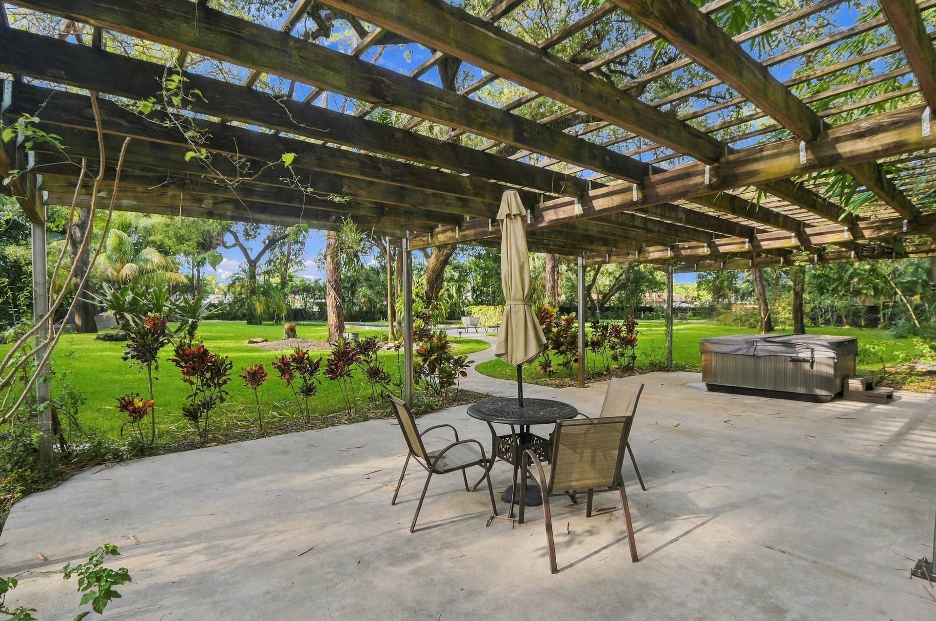 1549 SW 30th Place, Fort Lauderdale, FL 33315 Expansive concrete patio with a wooden pergola, lush green lawn, and mature trees