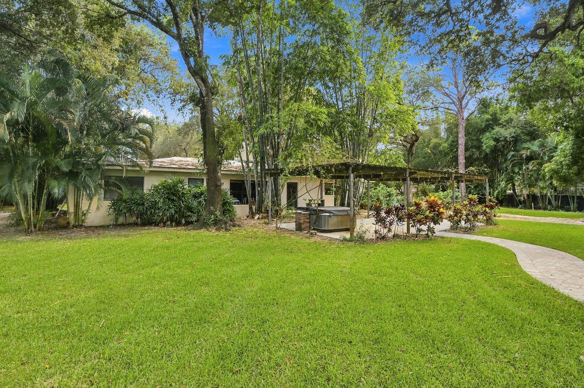 1549 SW 30th Place, Fort Lauderdale, FL 33315 Expansive lawn with mature trees, a curvilinear paver pathway, and a hot tub under a wooden pergola