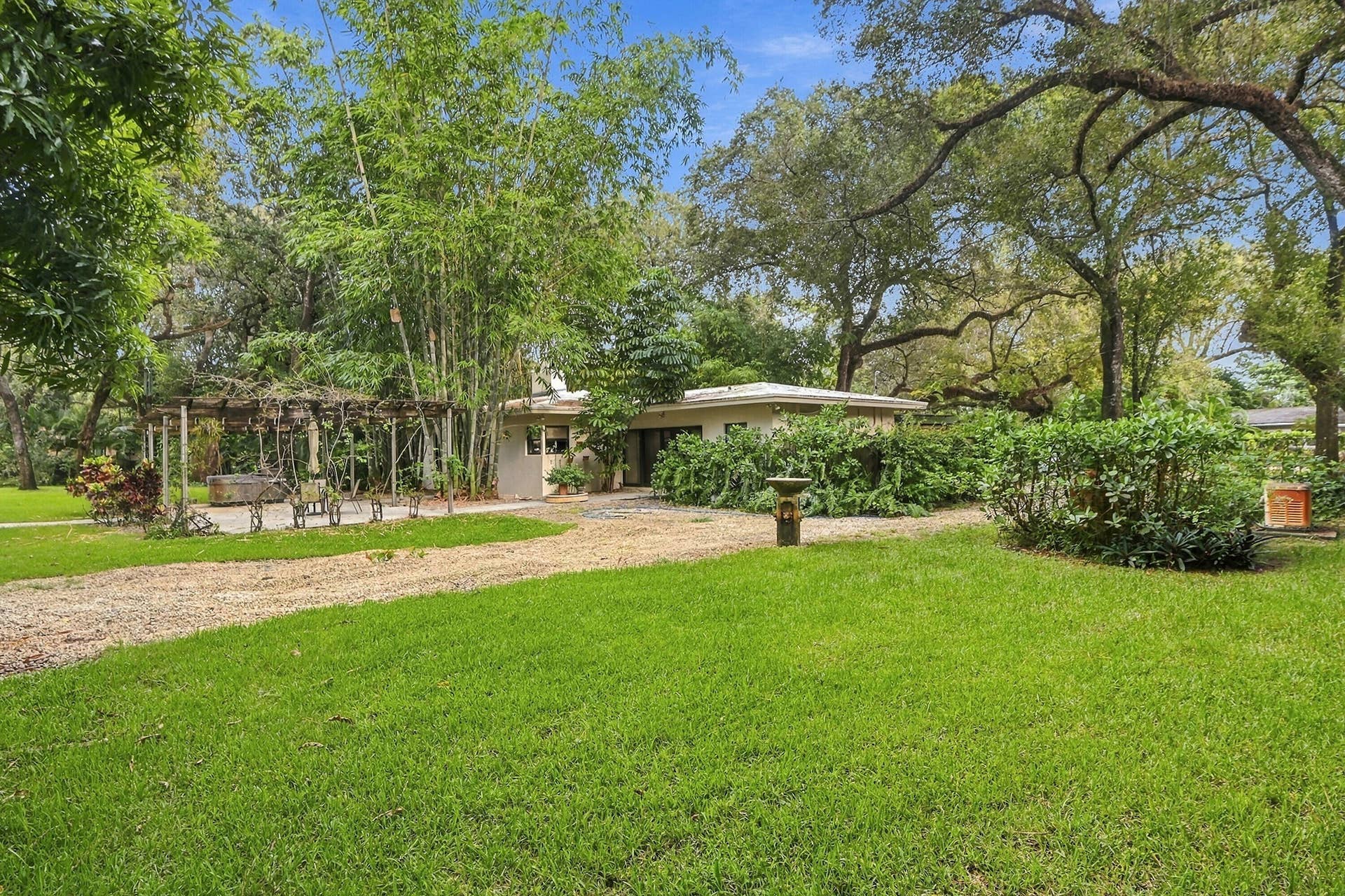 1549 SW 30th Place, Fort Lauderdale, FL 33315 Spacious lawn with a gravel driveway, mature trees, and a pergola structure