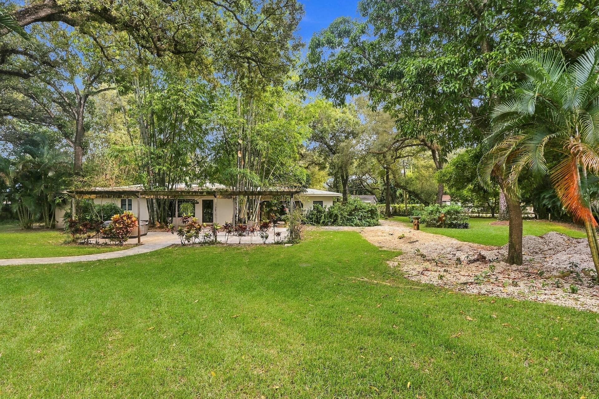 1549 SW 30th Place, Fort Lauderdale, FL 33315 Expansive green lawn with mature trees and a paved path leading to a home featuring an exterior patio with a pergola