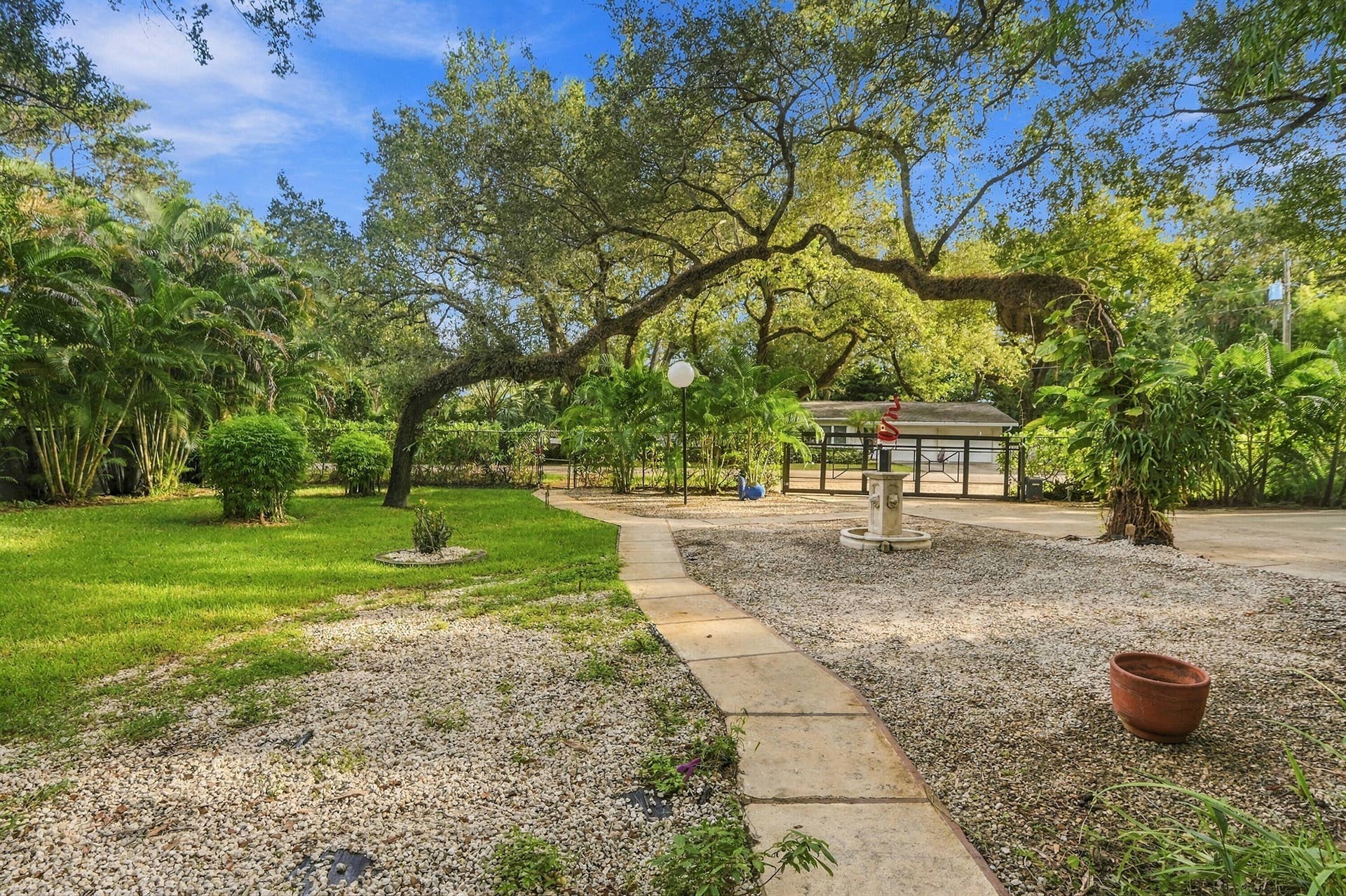 1549 SW 30th Place, Fort Lauderdale, FL 33315 Manicured lawn, mature trees, concrete paver pathway, gravel ground cover, and a central water feature