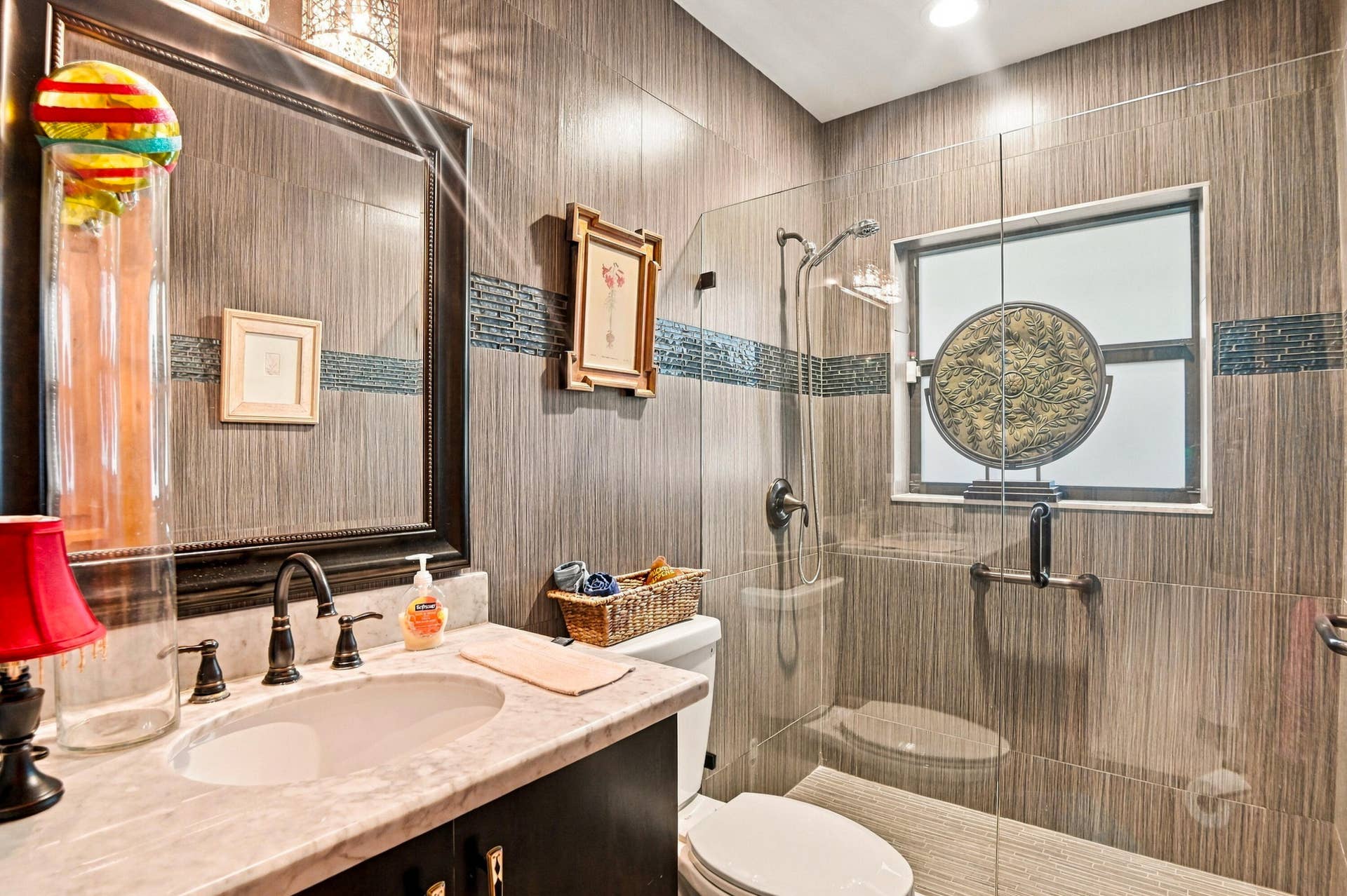 1549 SW 30th Place, Fort Lauderdale, FL 33315 Tile-finished walls featuring a decorative accent band, glass-enclosed shower, built-in vanity with a stone countertop, and an oval undermount sink with a bronze-finish faucet