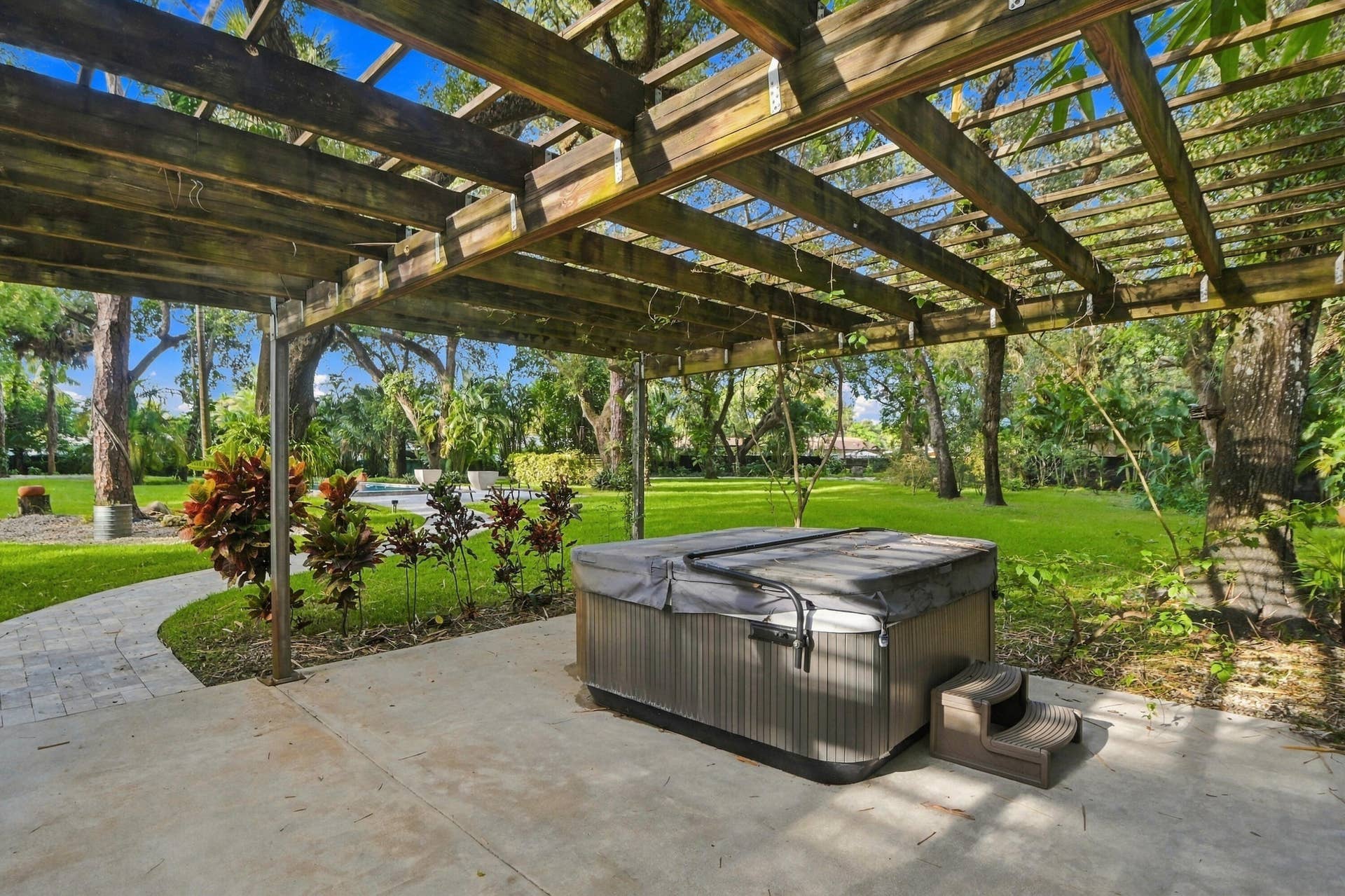 1549 SW 30th Place, Fort Lauderdale, FL 33315 Covered patio with a hot tub, concrete flooring, wood pergola, paver pathway, and manicured lawn