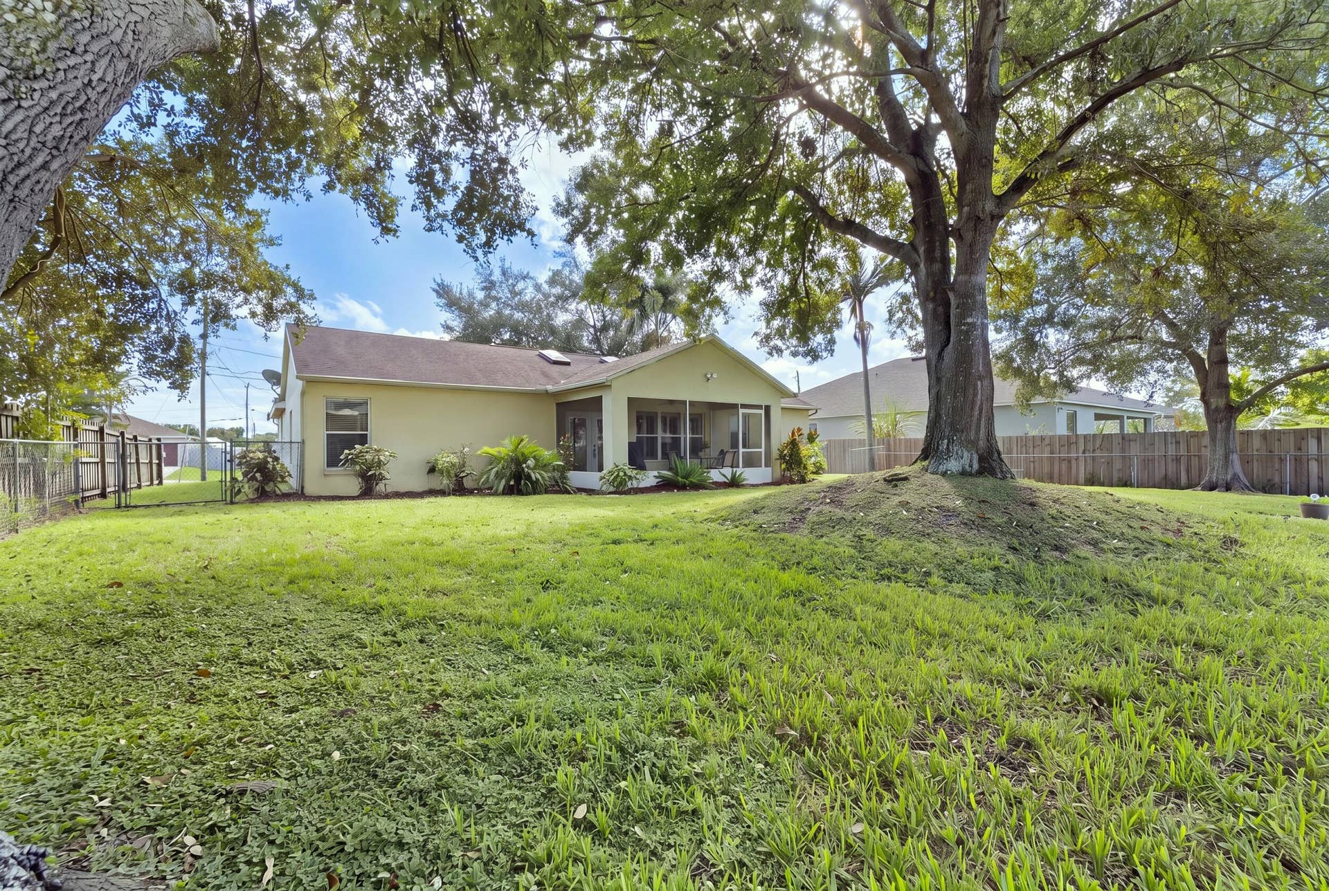 1649 SW ALVATON Avenue, Port St Lucie, FL 34953 Expansive backyard featuring a large mature tree, manicured lawn, perimeter wood fencing, and a covered screened-in patio
