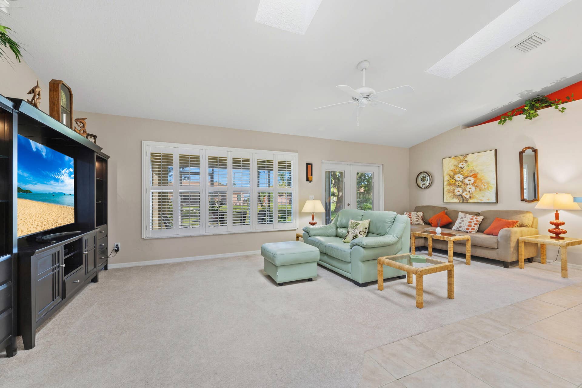 1649 SW ALVATON Avenue, Port St Lucie, FL 34953 Living area featuring a vaulted ceiling with skylights, white plantation shutters, and a ceiling fan