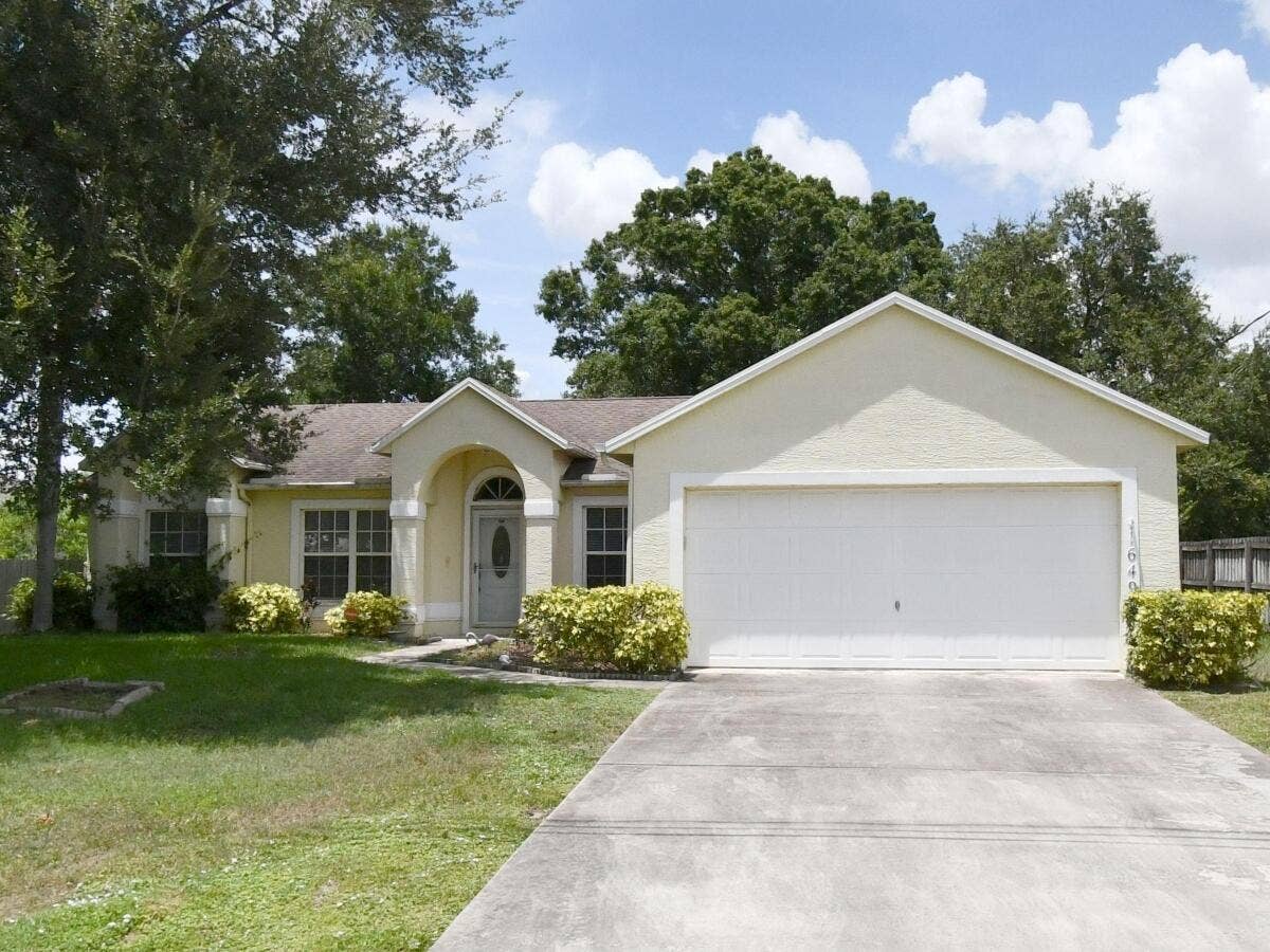 1649 SW ALVATON Avenue, Port St Lucie, FL 34953 Single-story residence featuring a stucco exterior, arched covered entryway, multi-pane windows, and an attached two-car garage