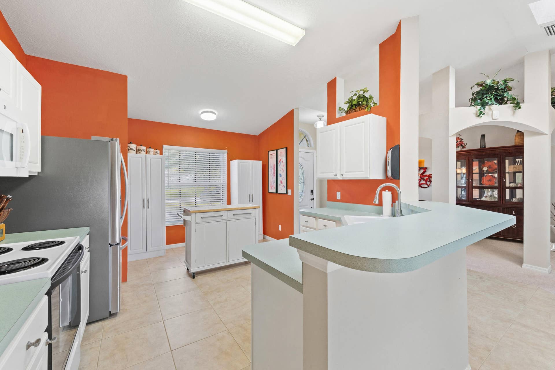 1649 SW ALVATON Avenue, Port St Lucie, FL 34953 Kitchen featuring white shaker-style cabinetry, breakfast bar, solid-surface countertops, tile flooring, and vaulted ceiling