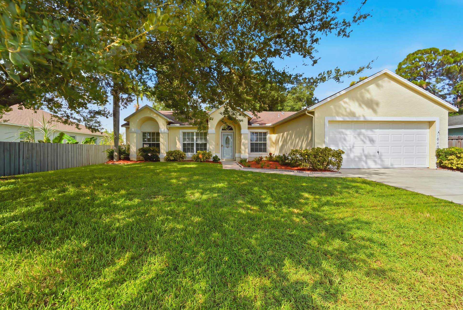 1649 SW ALVATON Avenue, Port St Lucie, FL 34953 Single-story residence featuring a stucco exterior, arched covered entryway, multi-pane windows, and an attached two-car garage