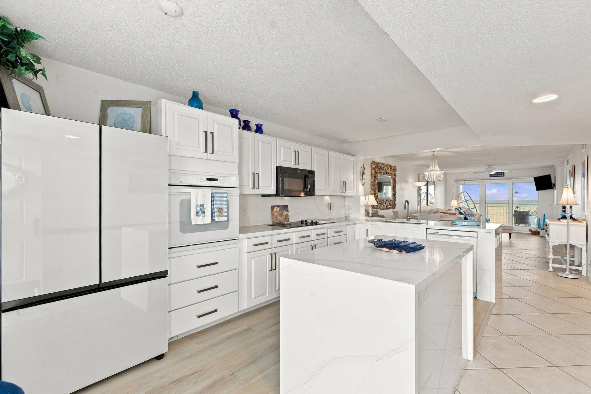 White cabinetry with dark hardware, built-in oven, integrated microwave, and a center island with a waterfall countertop