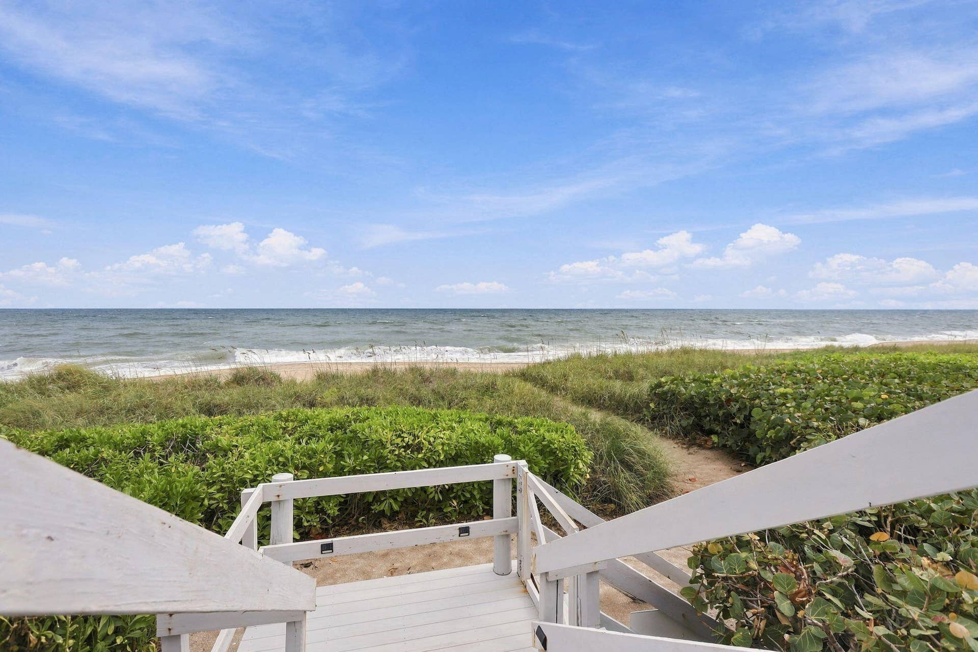 Waterfront access featuring a wooden boardwalk, white railings, and coastal vegetation
