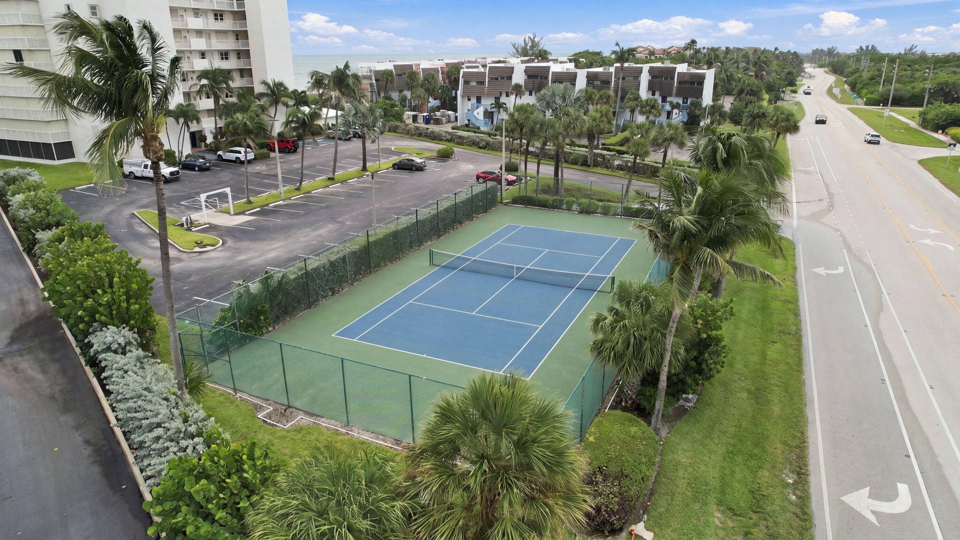 Tennis court with perimeter fencing, surrounded by mature palm trees and lush landscaping