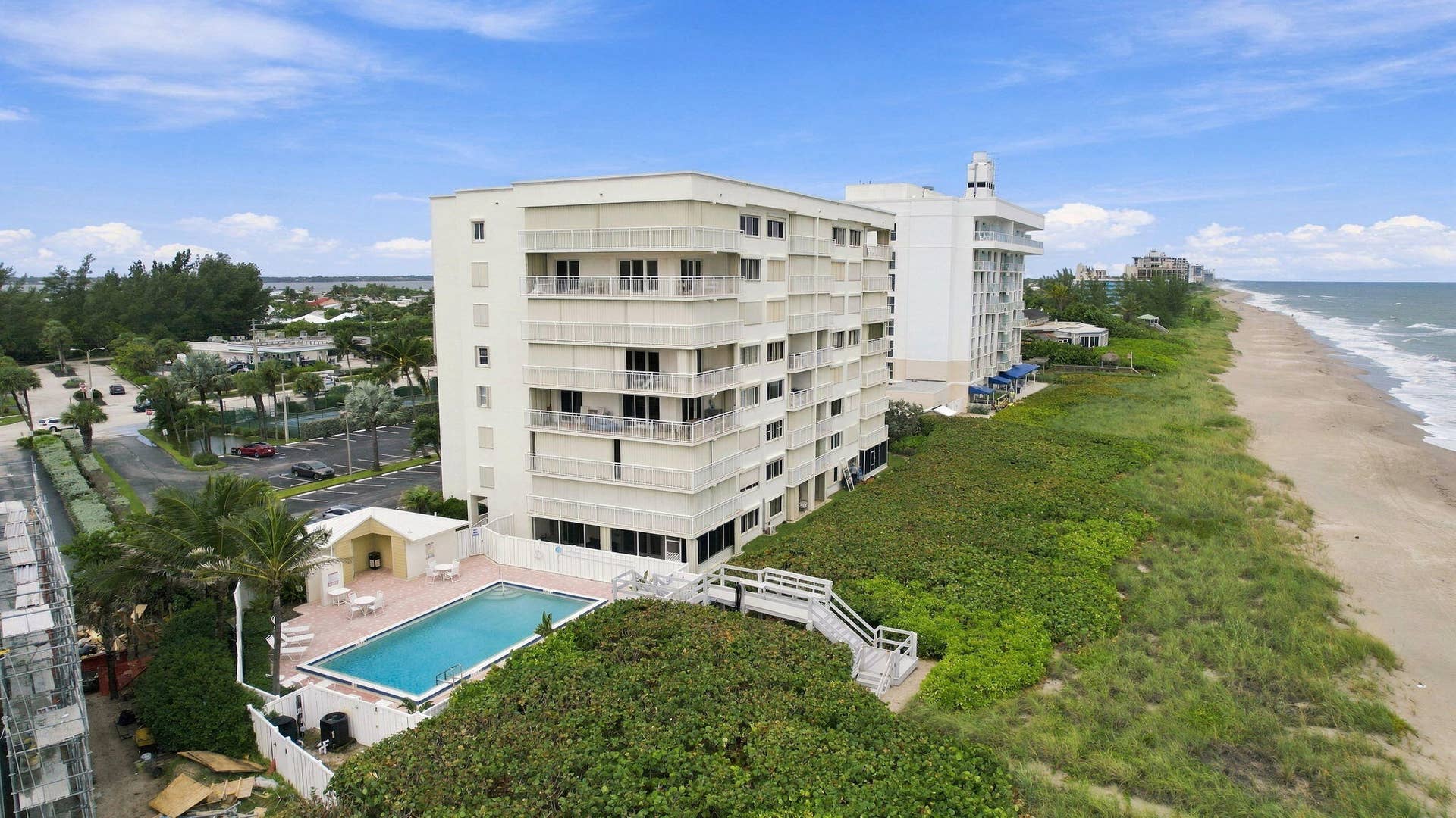 Multi-story condominium building featuring private balconies, a swimming pool, and direct beach access