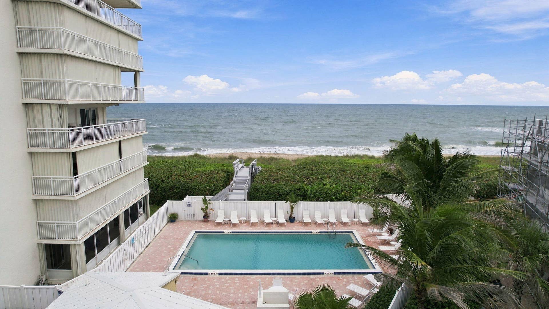 Oceanfront building featuring multiple balconies, a swimming pool, and a boardwalk leading to the beach