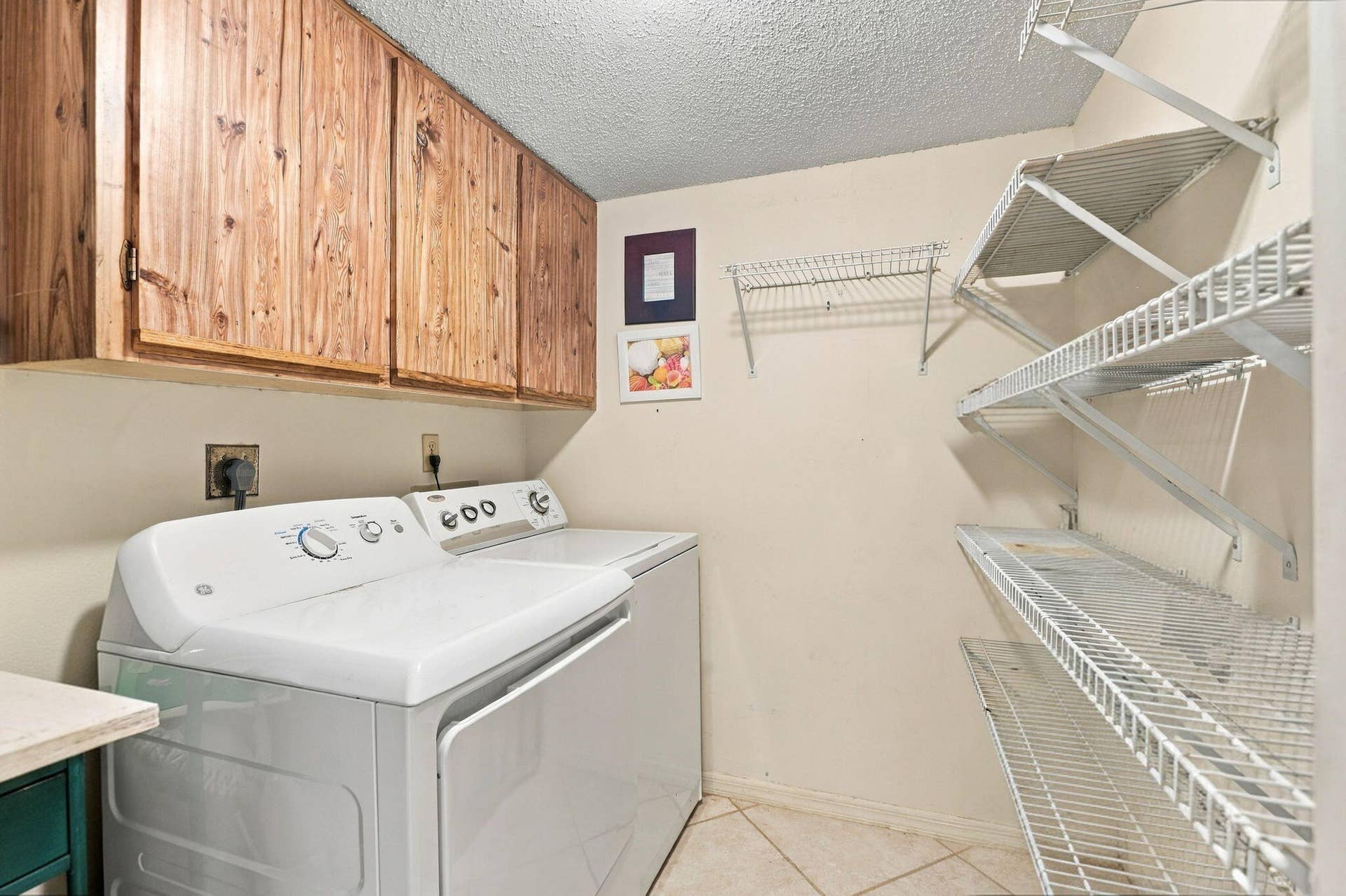 Wood-finish upper cabinetry provides storage above a laundry area with tile flooring and wire shelving