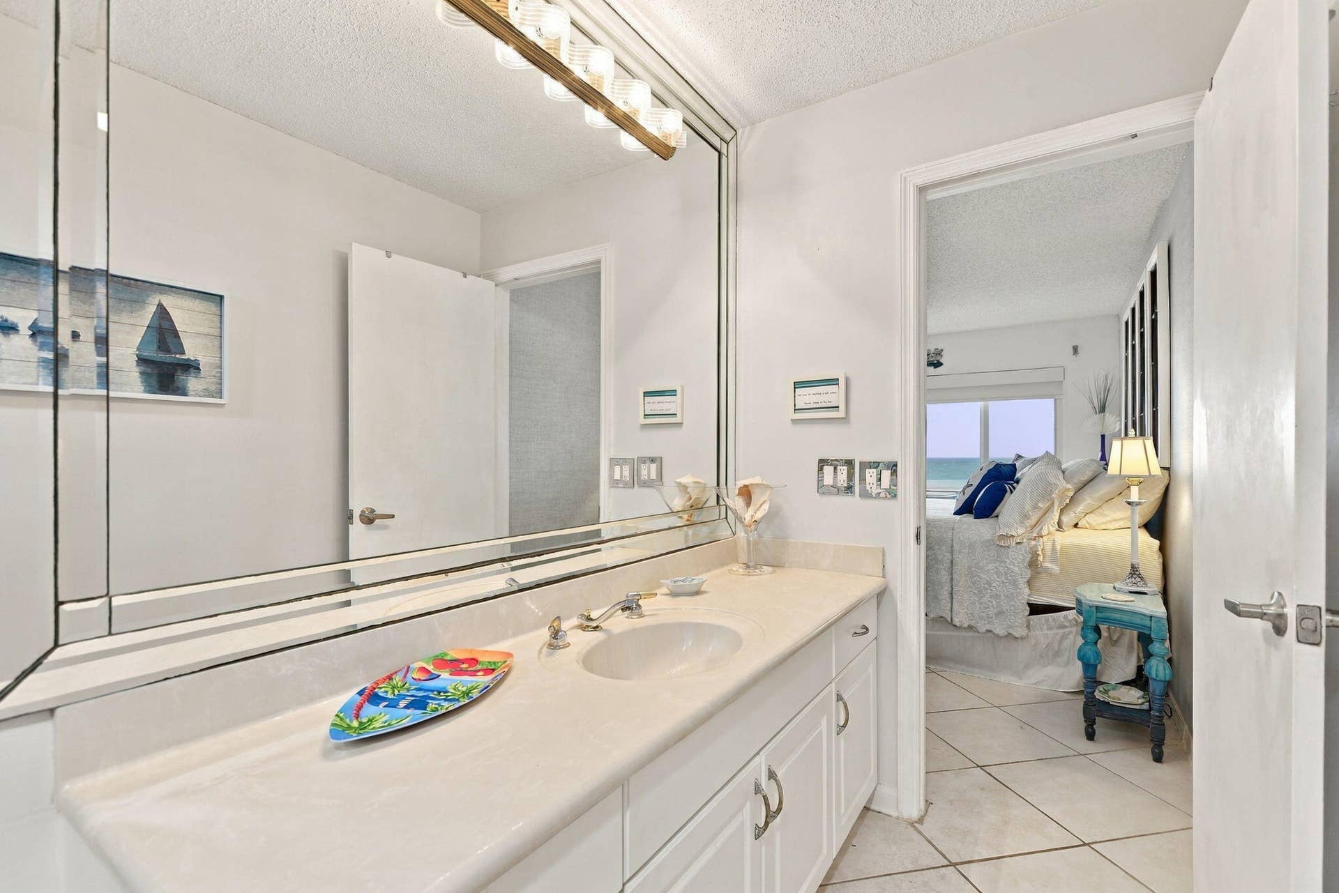 Bathroom with an expansive mirrored vanity and integrated sink, complemented by white cabinetry with polished hardware