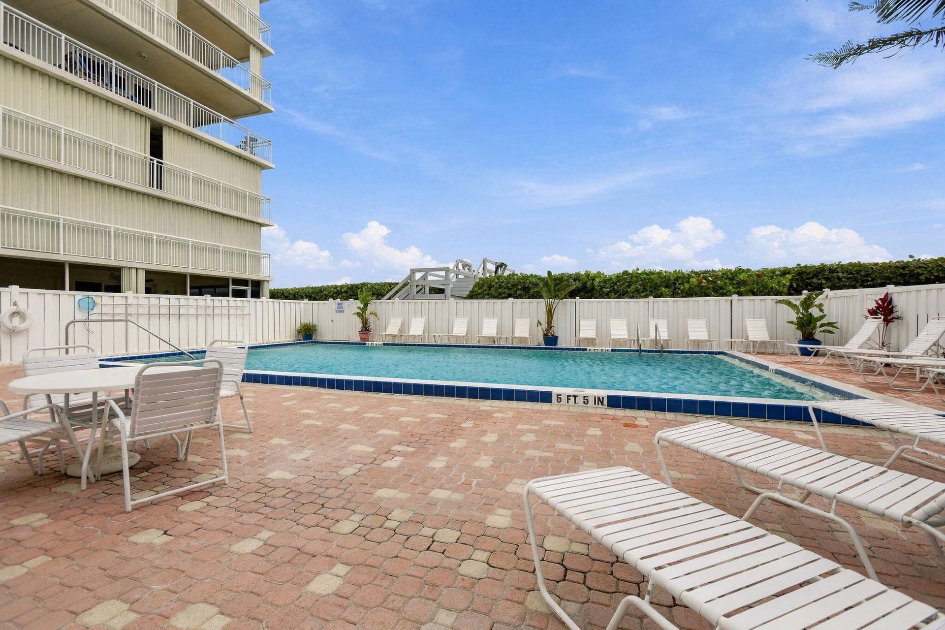 Swimming pool with a blue tile border, surrounded by a paver patio and white fencing