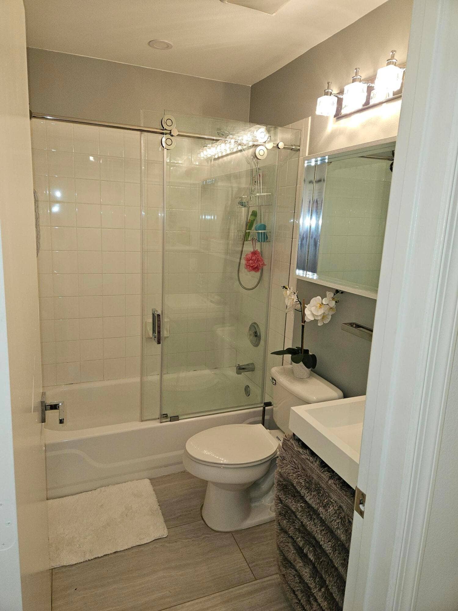 1460 SW 47TH Avenue, #1460, Deerfield Beach, Deerfield Beach, FL 33442 Tub-shower combination with sliding glass doors, contemporary vanity with integrated sink, modern lighting fixture, and large format floor tiling
