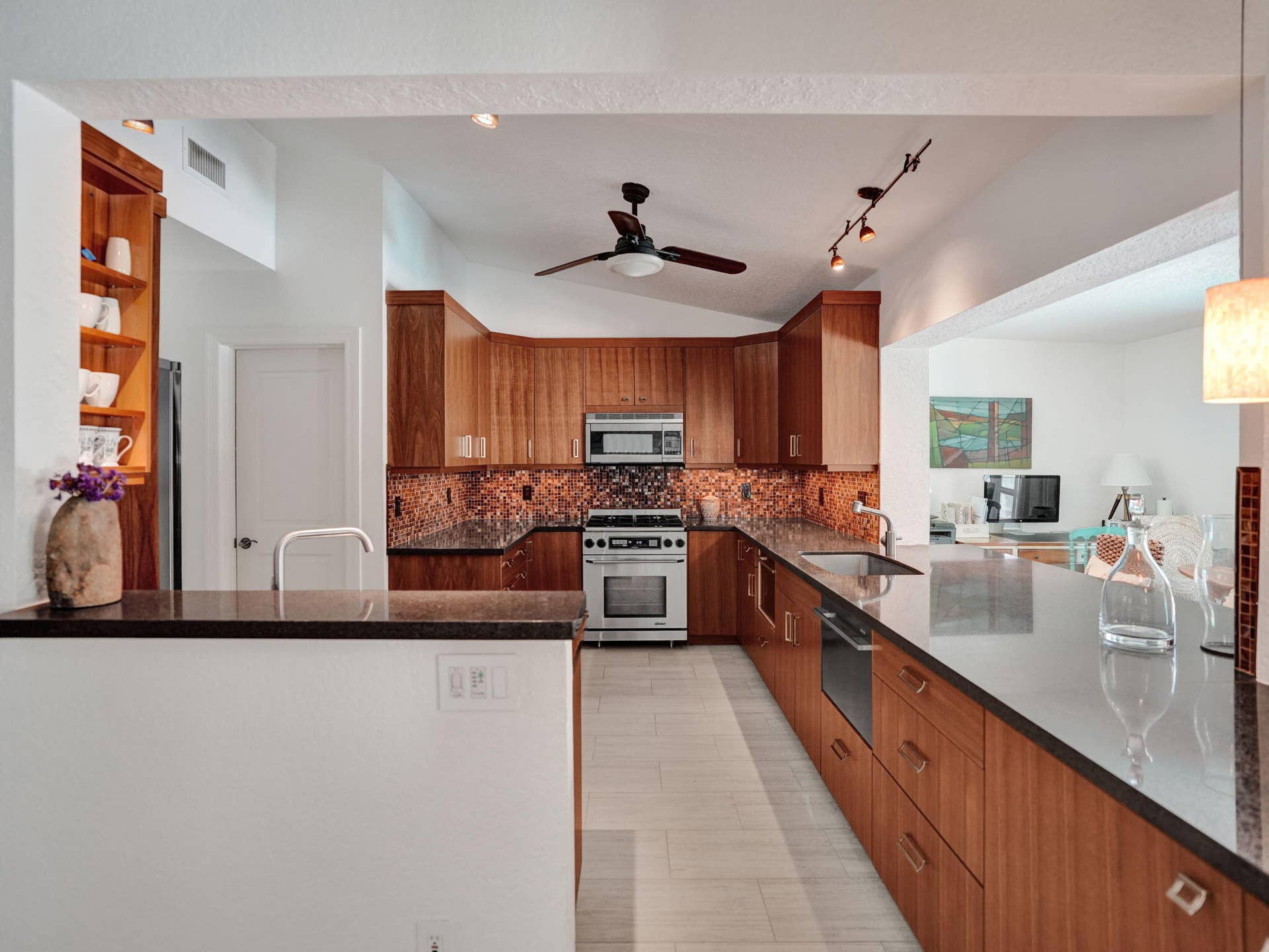 Kitchen featuring rich wood cabinetry, stainless steel appliances, a tile backsplash, dark countertops, and track lighting
