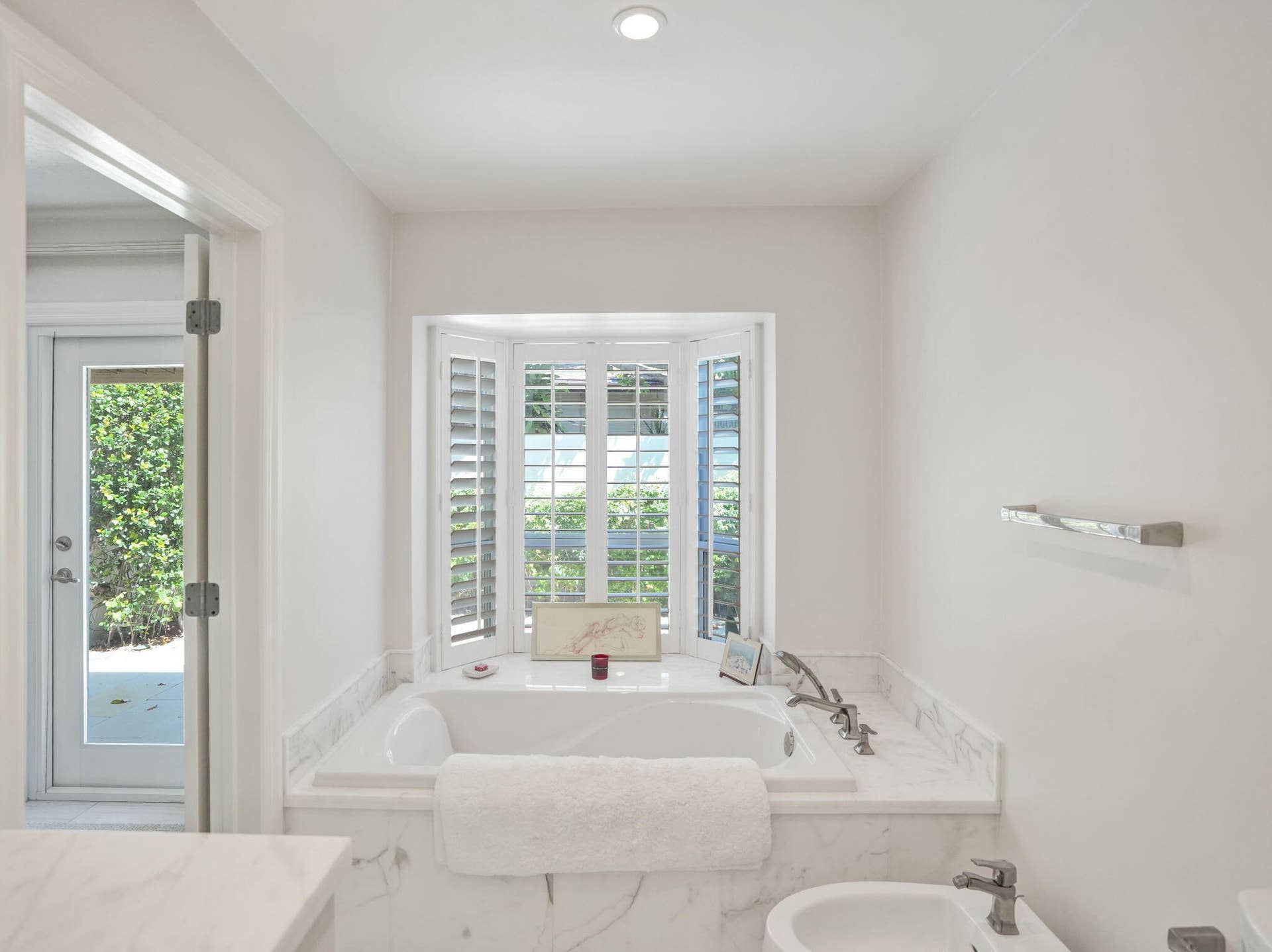 Recessed lighting, bay window with plantation shutters, built-in soaking tub with marble surround, polished chrome fixtures, and bidet