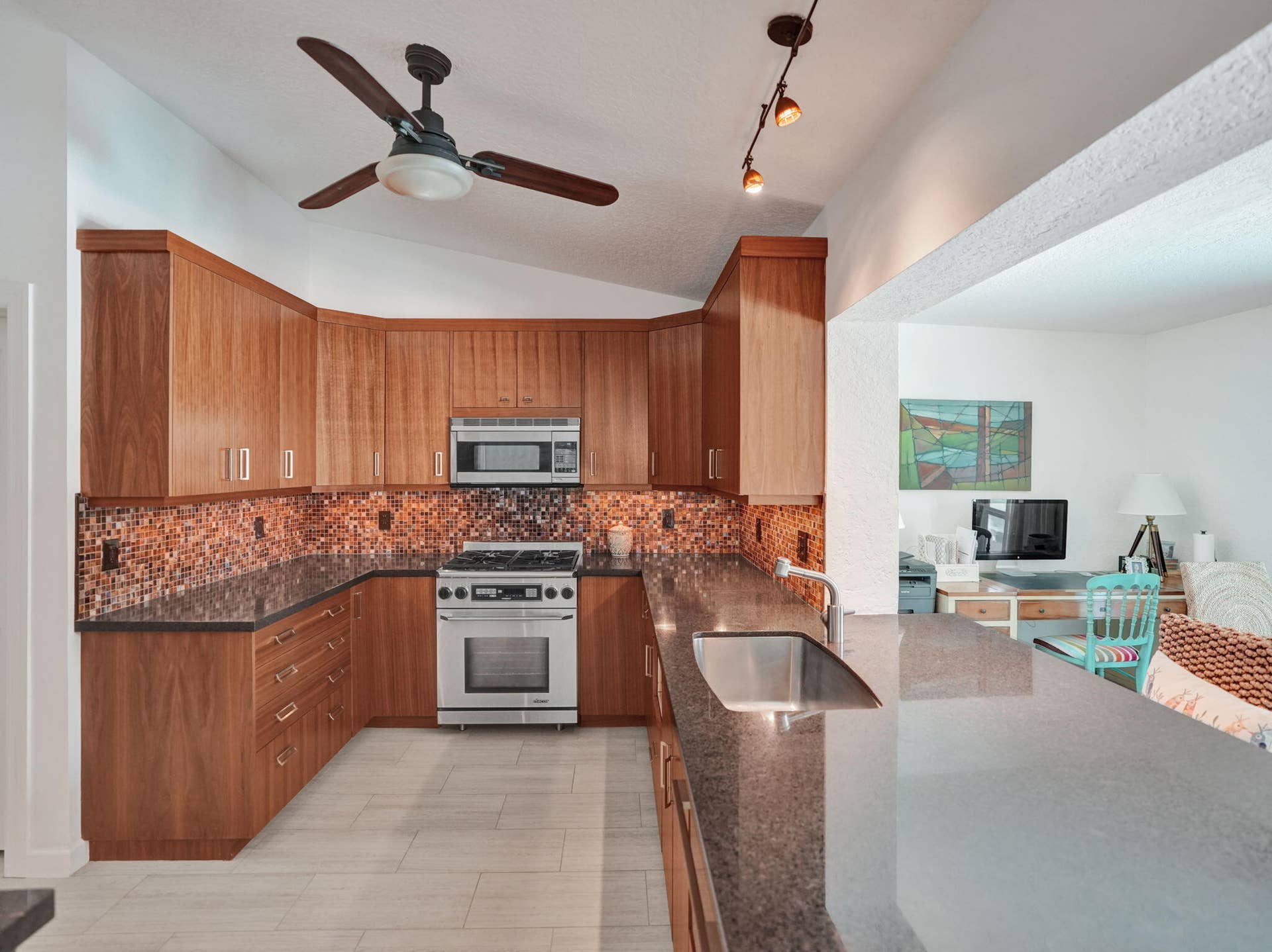 Kitchen featuring wood-finish cabinetry, mosaic tile backsplash, stainless steel range, and an integrated stainless steel sink within a stone countertop
