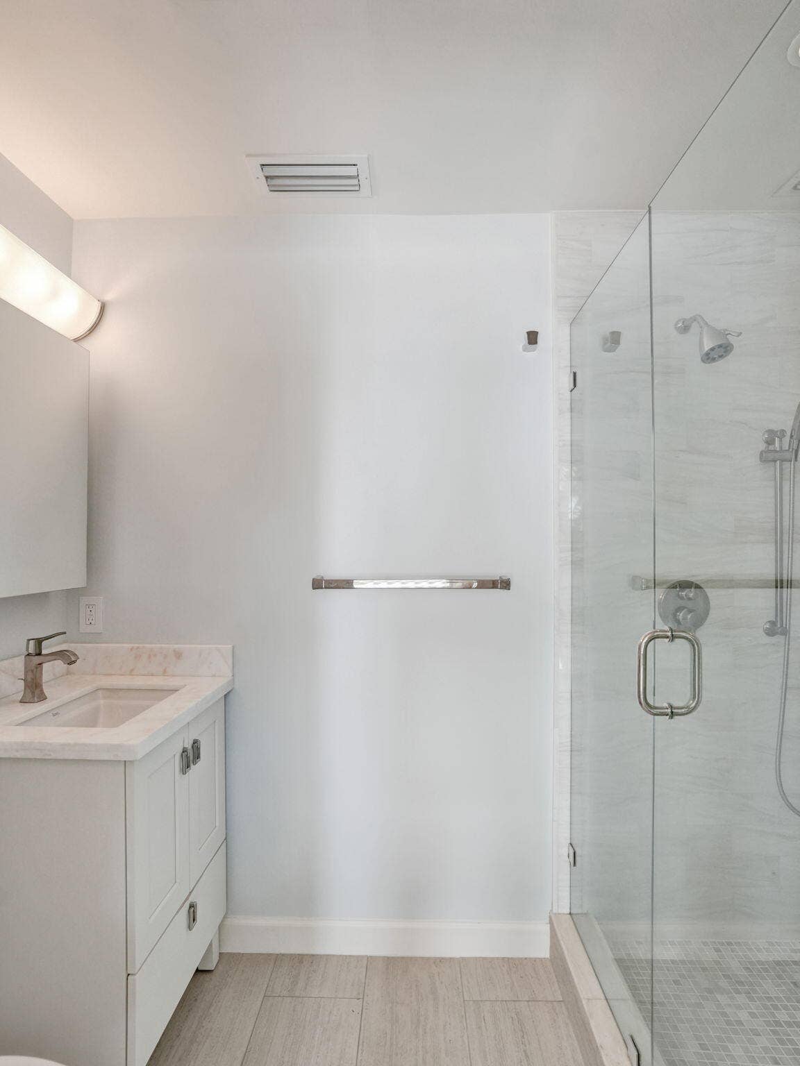 White vanity with brushed nickel faucet, glass-enclosed shower, white tile shower surround, and wood-finish flooring