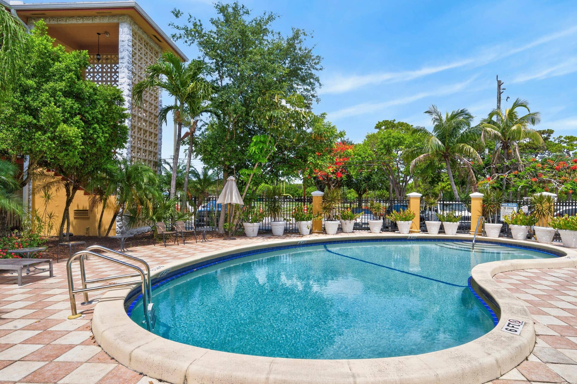 744 NE 14th Avenue, #21, Fort Lauderdale, FL 33304 Lagoon-style resort pool with curved perimeter and sun shelf, surrounded by decorative brick paver decking and mature tropical landscaping including palms and flowering trees