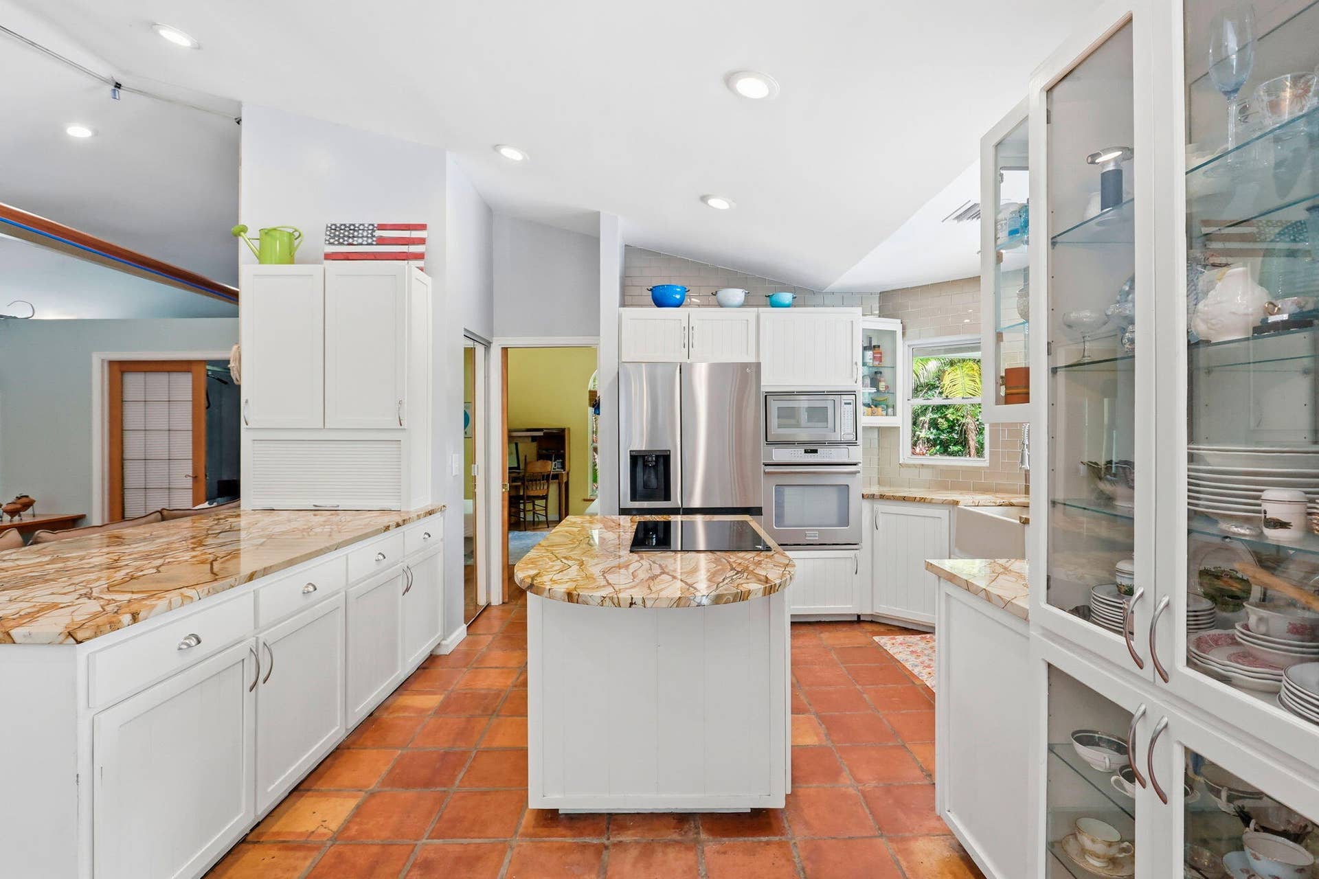 Kitchen featuring an island, white cabinetry, integrated stainless steel appliances, natural stone countertops, and terra cotta tile flooring